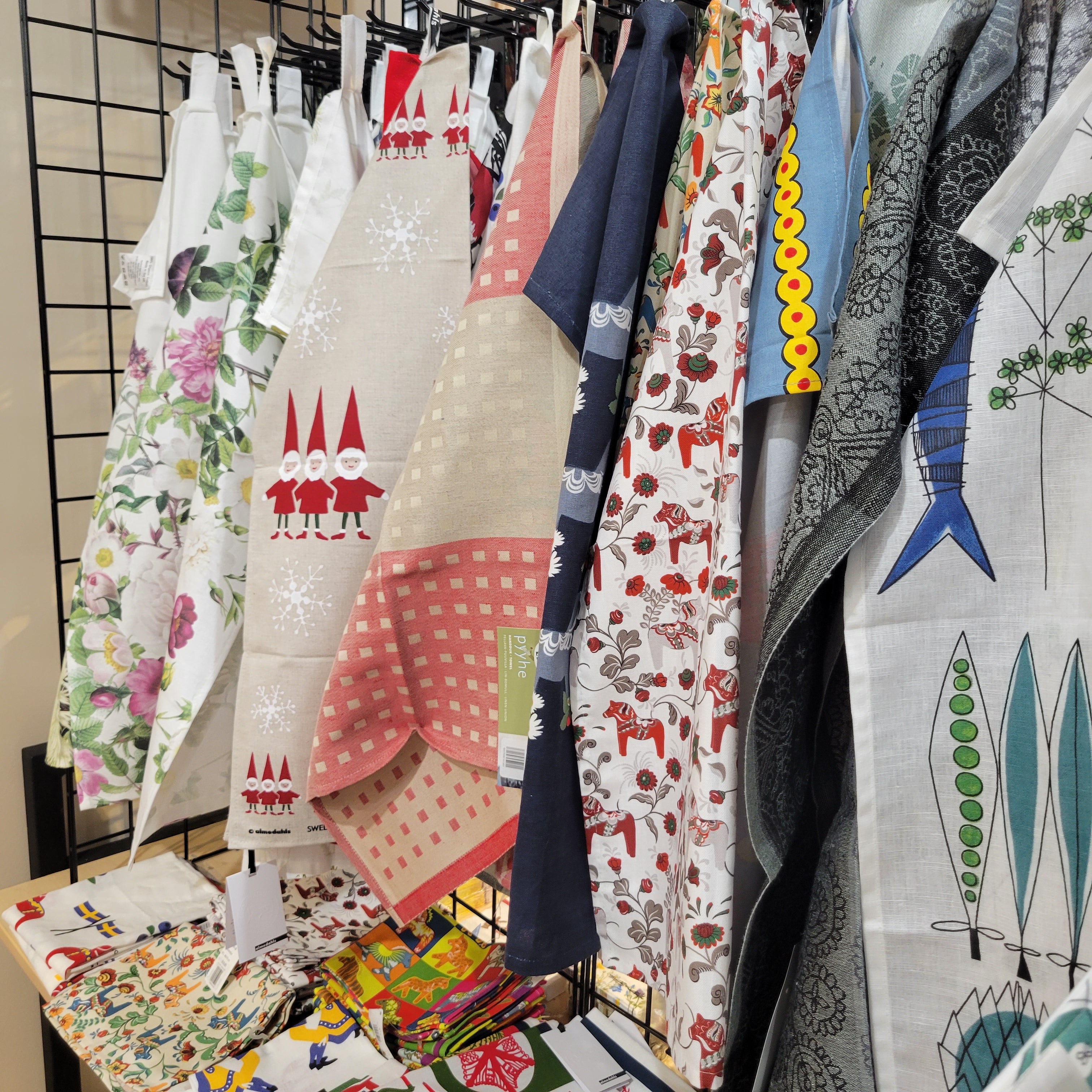 A display of colorful printed textiles with various patterns, including gnomes, florals, and abstract designs, hanging on a metal rack.