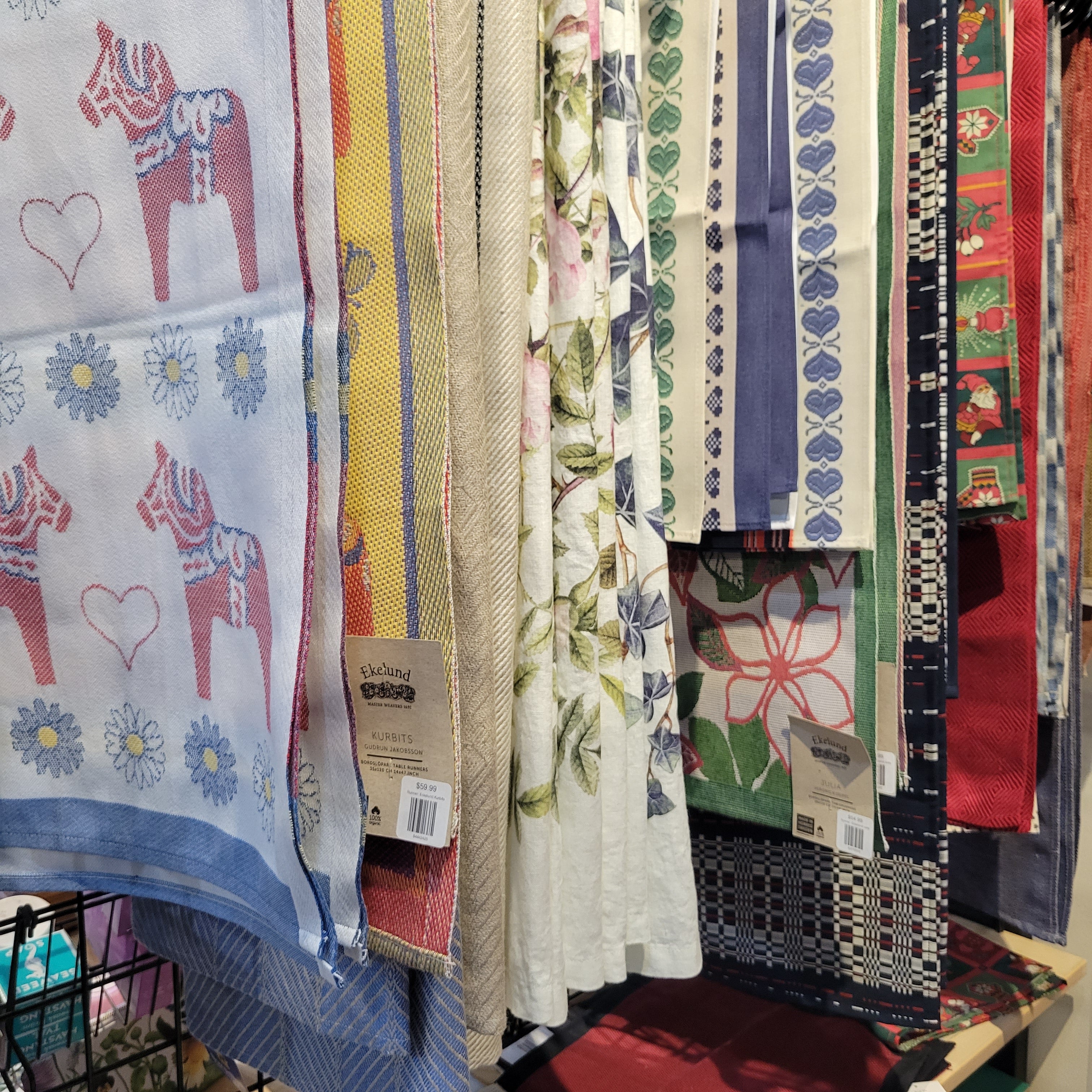 A display of various patterned textiles, including designs with hearts, floral prints, and geometric patterns, hanging vertically.
