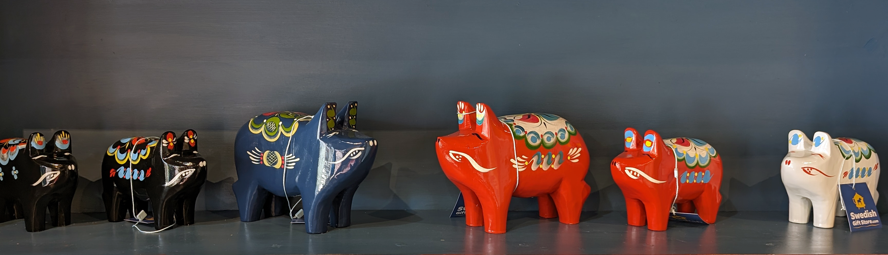 A row of colorful painted horse figurines on a blue shelf, featuring black, blue, and red colors with decorative patterns.