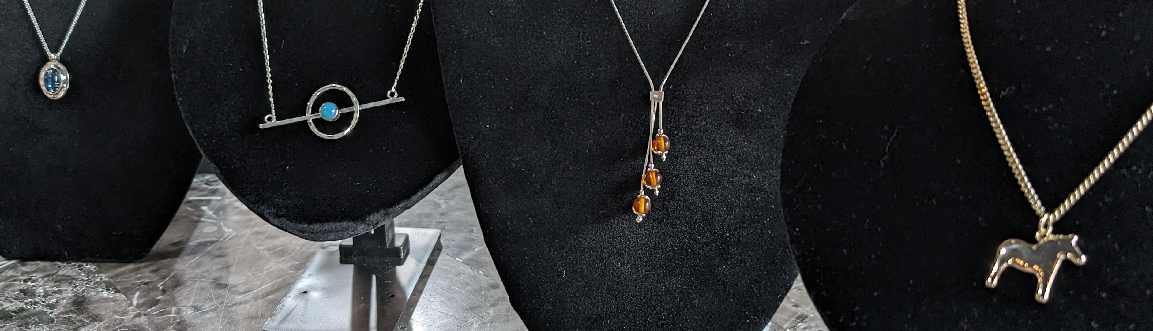 Four necklaces on black display stands featuring various designs, including gemstones and a horse pendant.