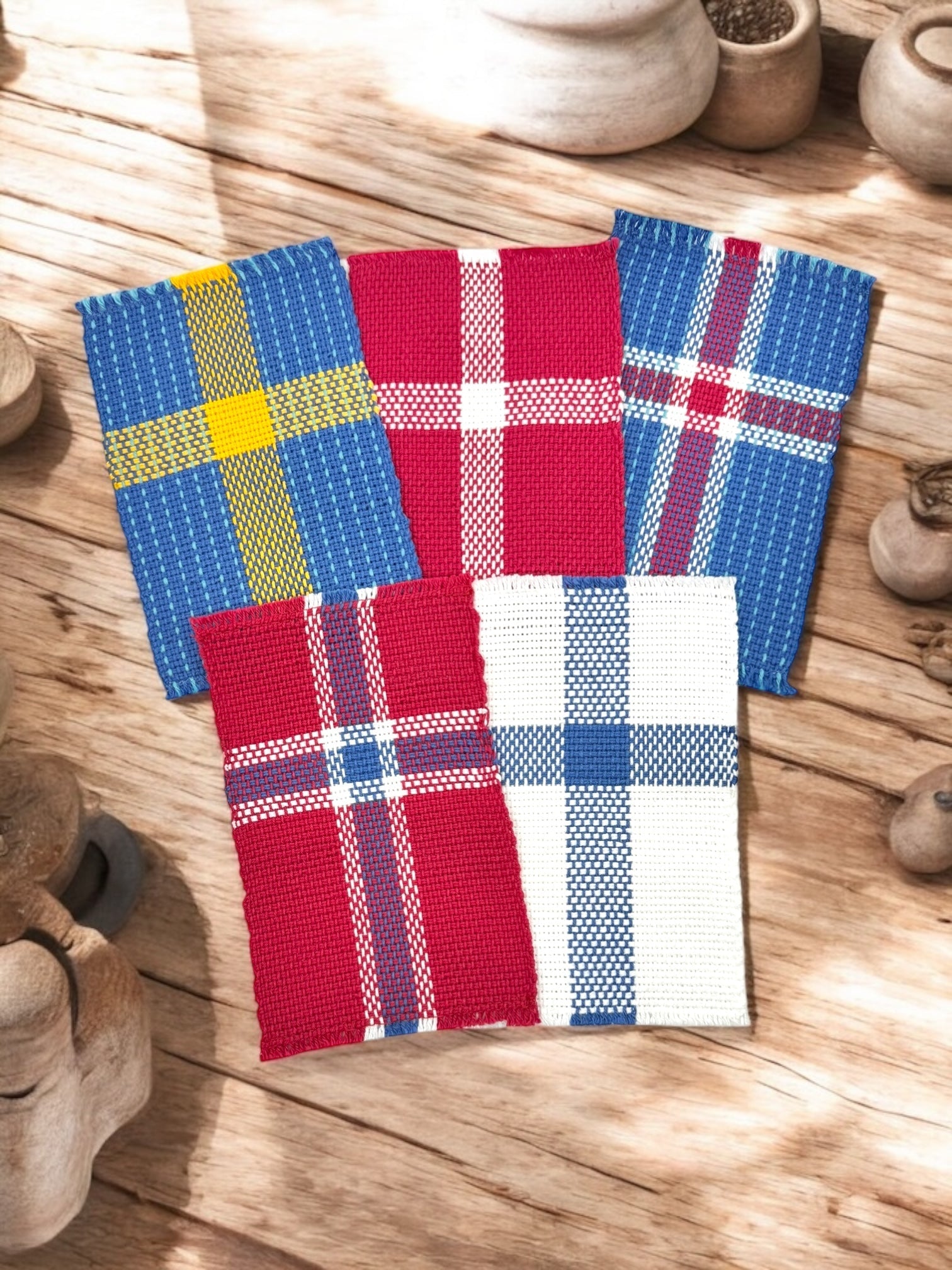 Five rectangular woven fabric swatches with varied plaid patterns and colors, arranged on a wooden surface with carved wooden objects around them.