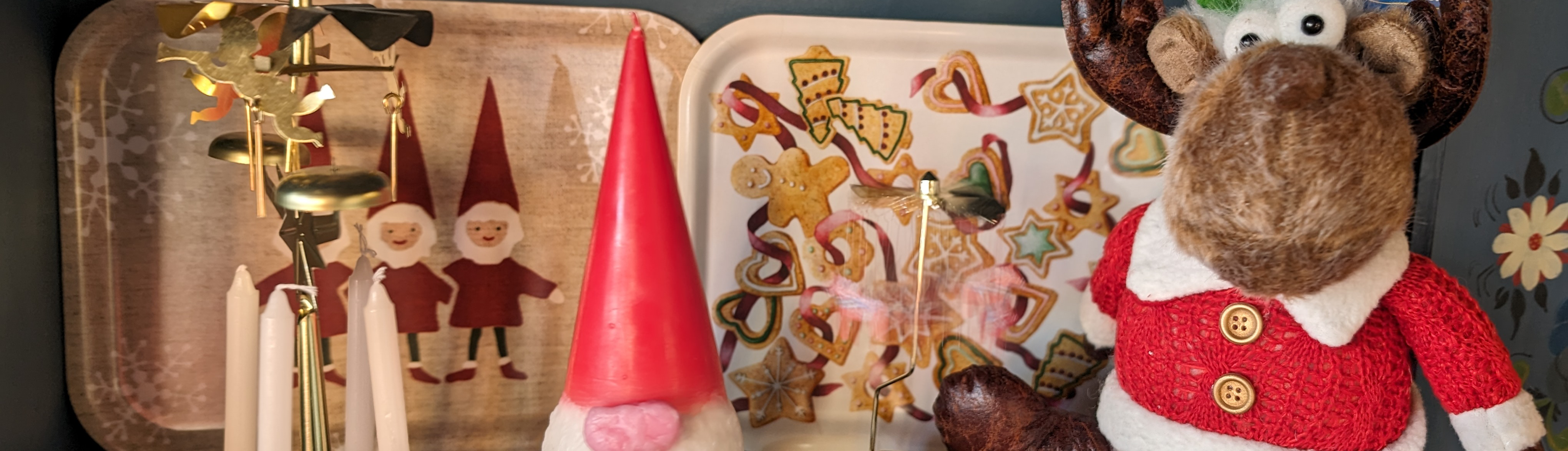 Festive display featuring a reindeer figurine, red-cloaked gnome, candle carousel, and colorful cookies on trays with holiday-themed designs.