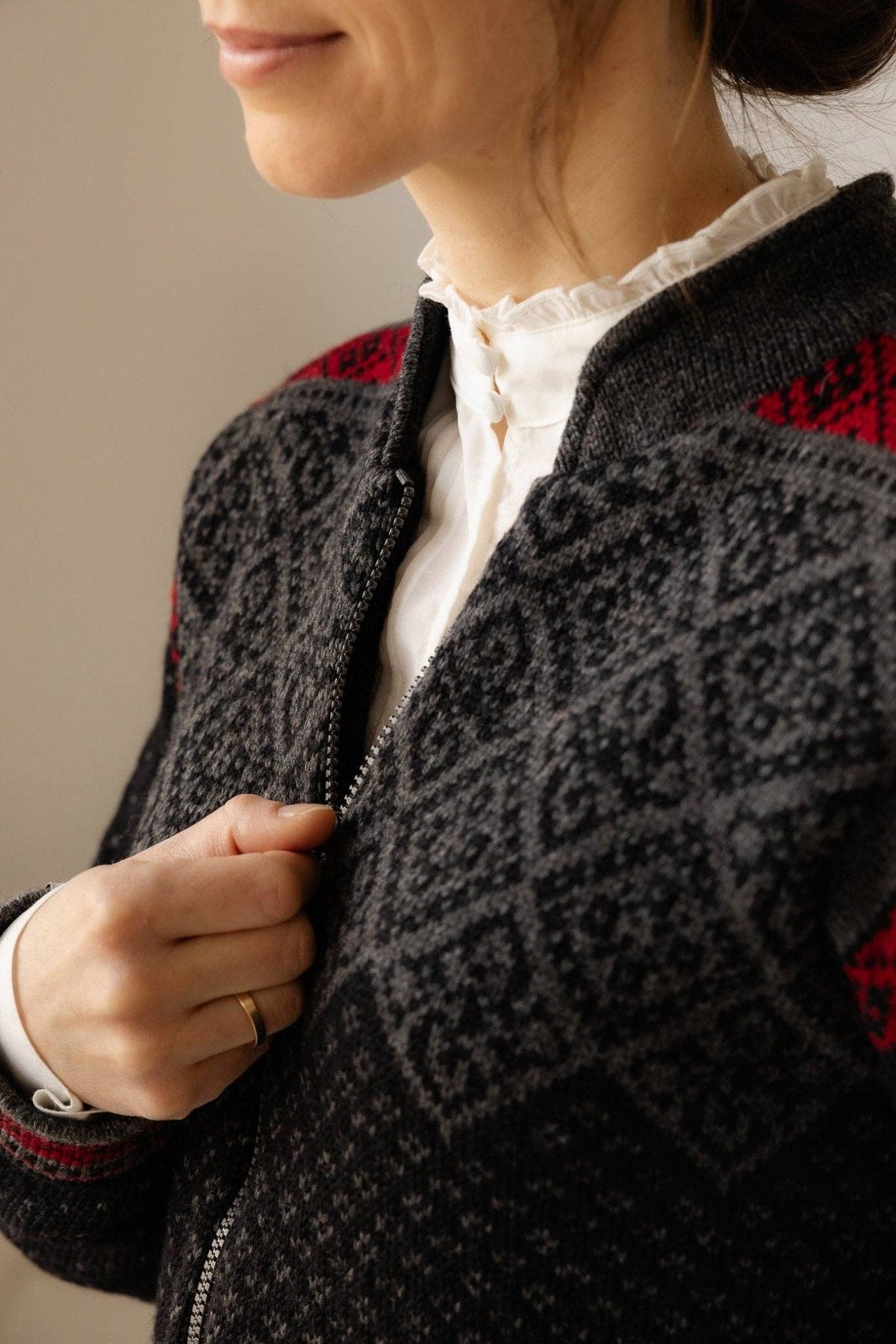 A person zipping a grey and black patterned Norwegian wool cardigan with red shoulder accents and a fleece-lined collar.