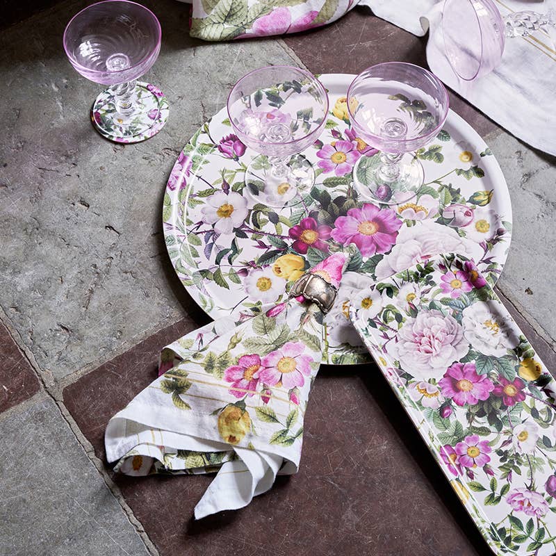 A Koustrupco Denmark Rose Flower Garden round serving tray (14.9) is arranged with a rectangular plate, matching napkins, and three empty pink-tinted glasses on a stone tile floor.