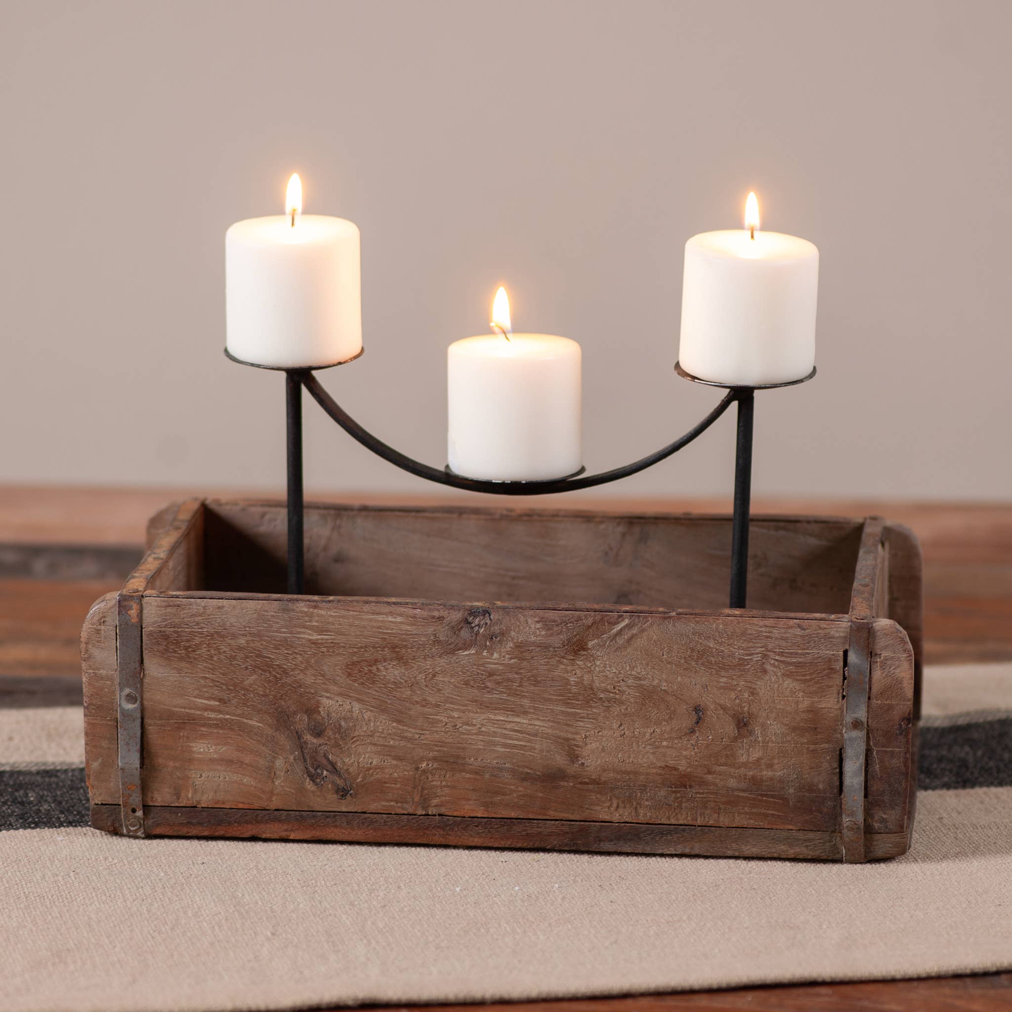 The Candle Holder: Vintage Wooden Brick Mold with Fancy Raised Ball Candle Holders features three white pillar candles at varying heights on black stands, creating a charming reclaimed wood centerpiece.