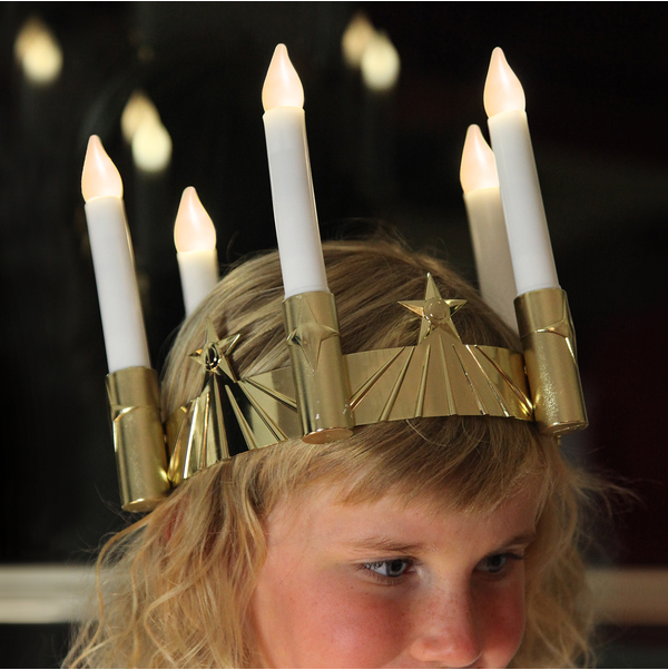 A child wears the St Lucia Crown by Star Trading of Sweden, featuring five upright, battery-operated flameless LED candles.