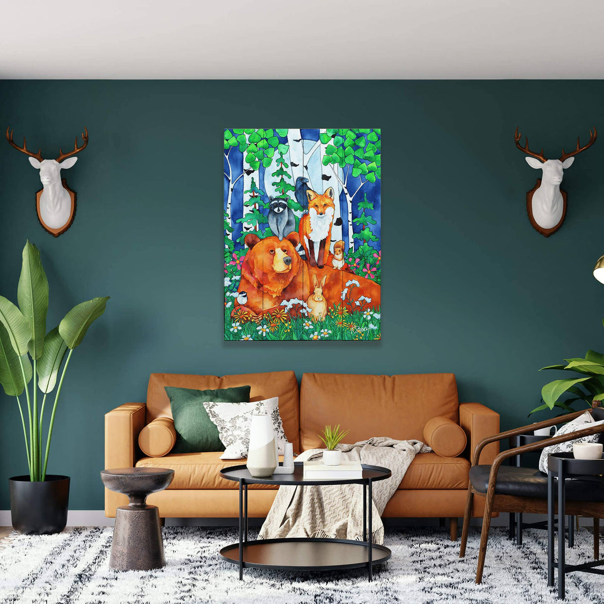 A living room with a brown sofa and green accent wall features the 'Creatures Great and Small' 17" x 23" wood panel wall art and two white deer head wall mounts.