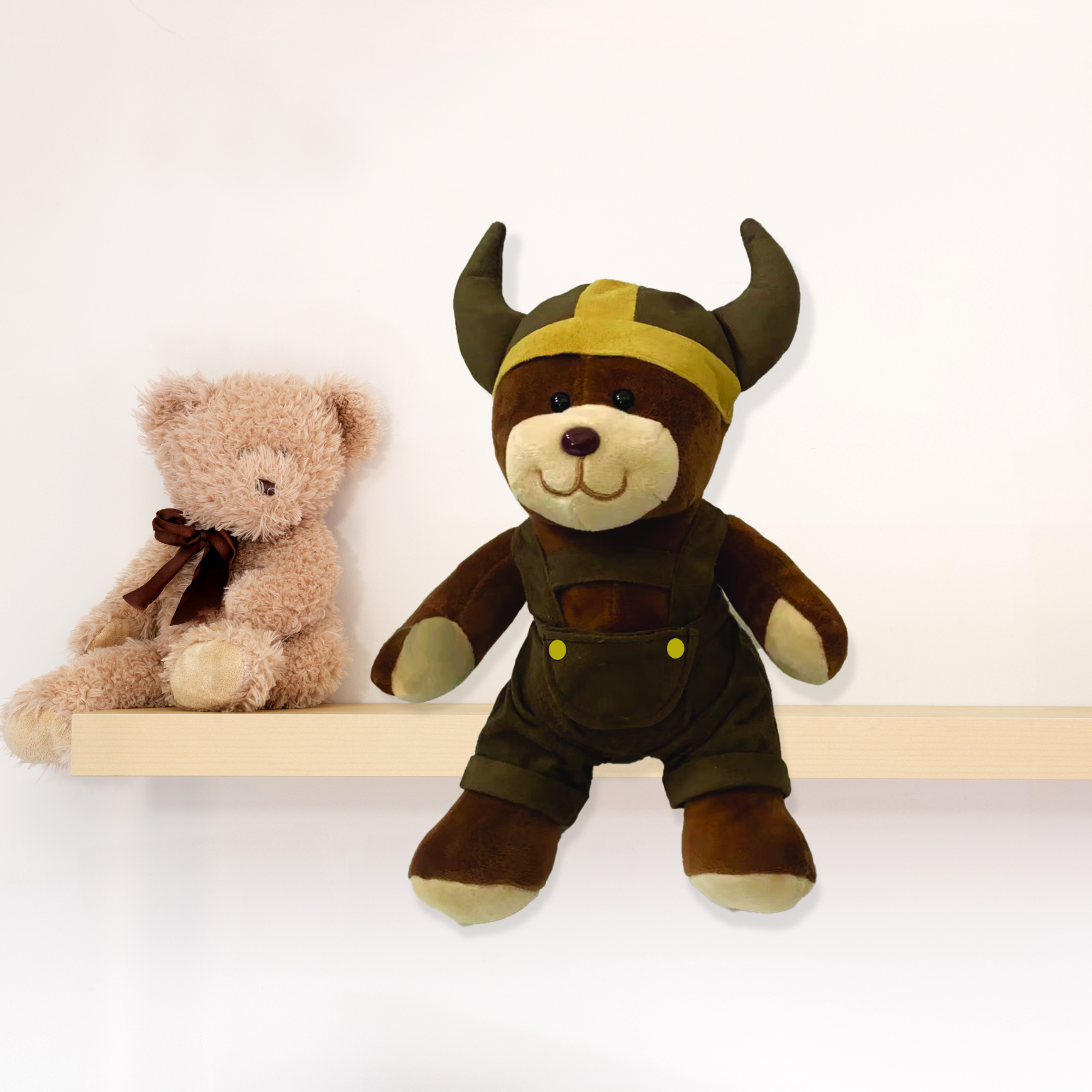 A light brown teddy bear with a ribbon sits beside the Plush: Viking Boy Teddy Bear wearing a horned Viking helmet on a wooden shelf.