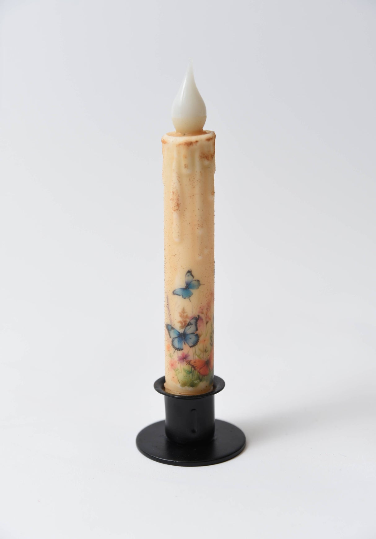 Butterfly Panorama LED Timer Taper Candle, top dusted and cream-colored with floral and butterfly designs, stands in a black holder against a plain white background.