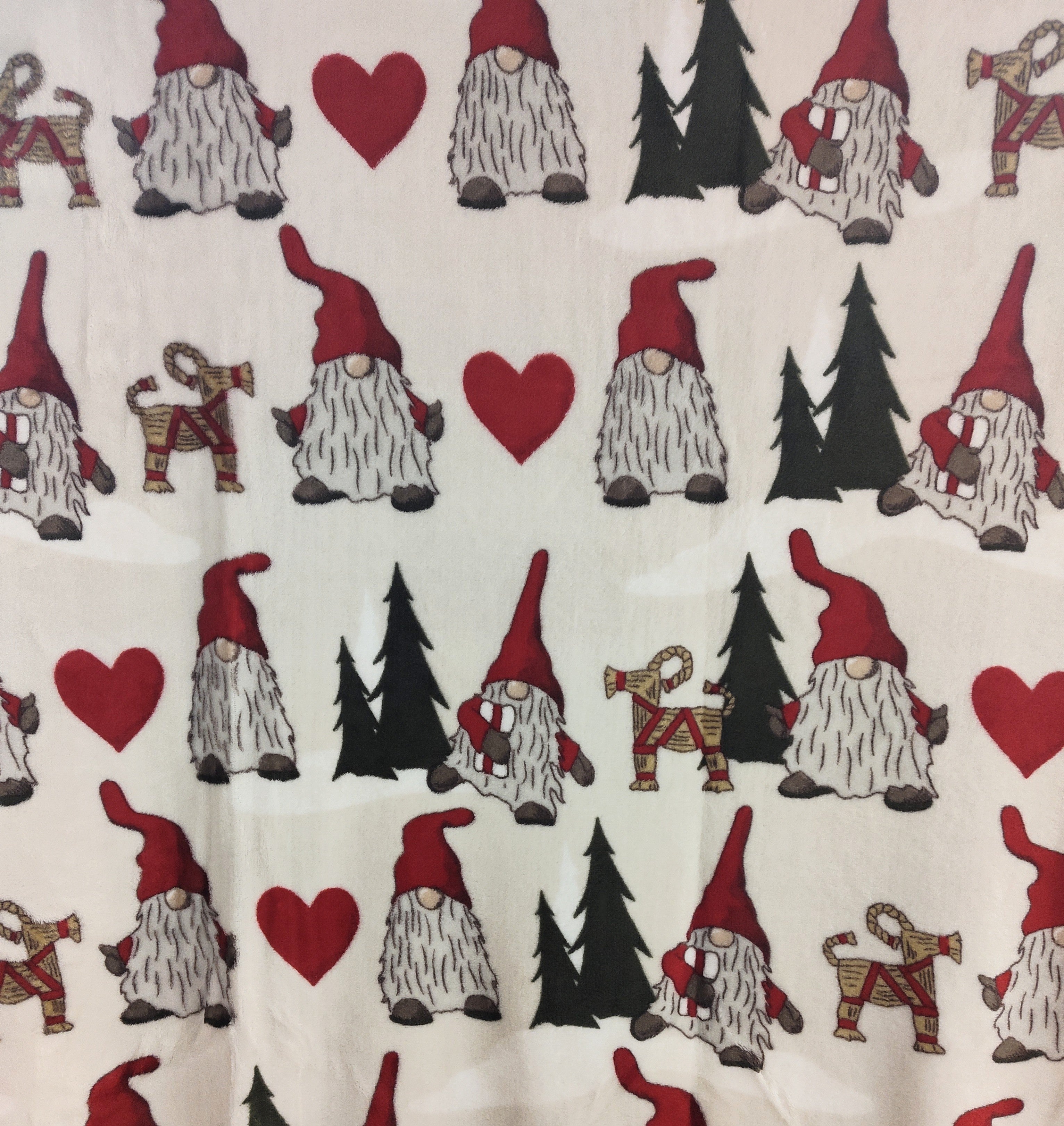 The Redlunds Noel Throw Blanket (130 x 170 cm) features a light background with gnomes in red hats, red hearts, green trees, and red-and-yellow straw goats—perfect for a cozy Scandinavian touch.