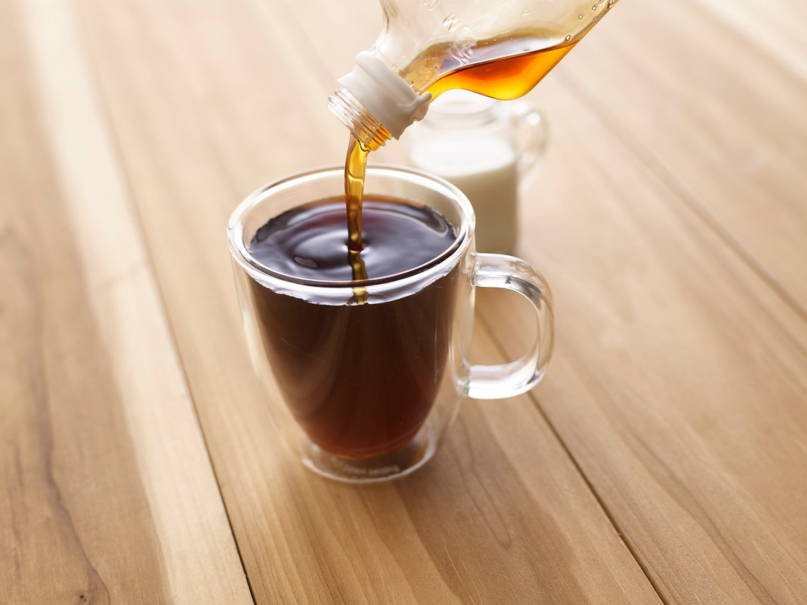 On a wooden table, pour Summer Favorites Maple Syrup: Bourbon Barrel (6.8 oz) into a glass mug, with a small pitcher of cream nearby, perfect for drizzling over desserts.