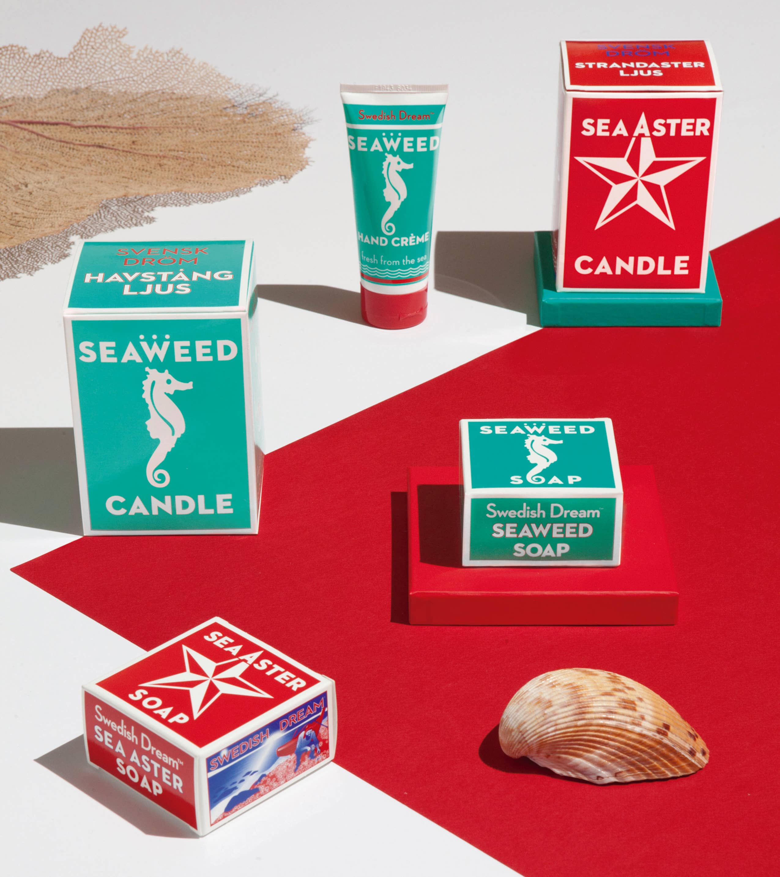 A calming arrangement featuring the Sea Aster Soap from Swedish Dream, along with soothing candles, is displayed on a red surface beside a seashell and dried leaf.