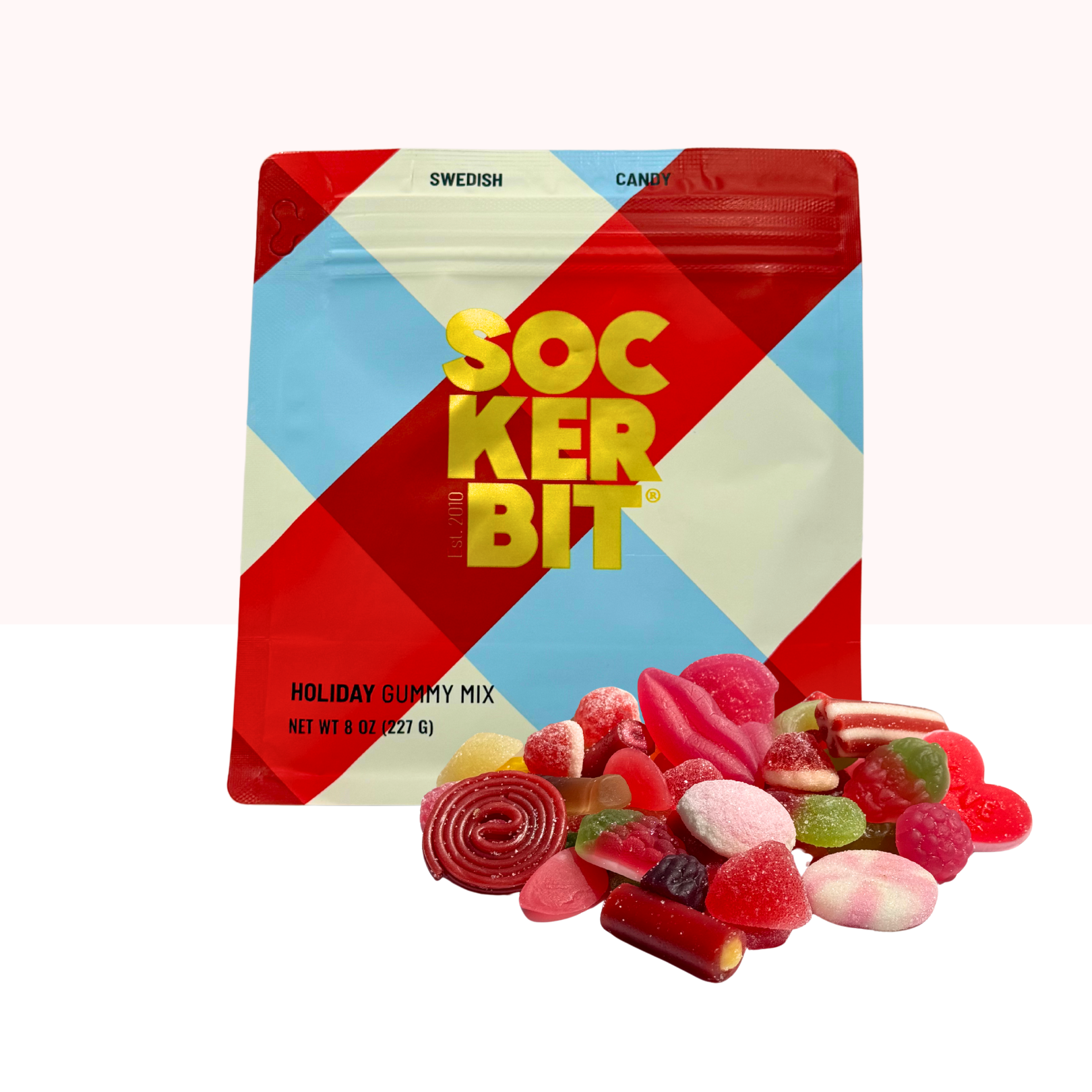 An 8oz Candy: Holiday Mix Pouch bag sits behind an assortment of colorful sweet and sour gummies, arranged in front of the festive package.