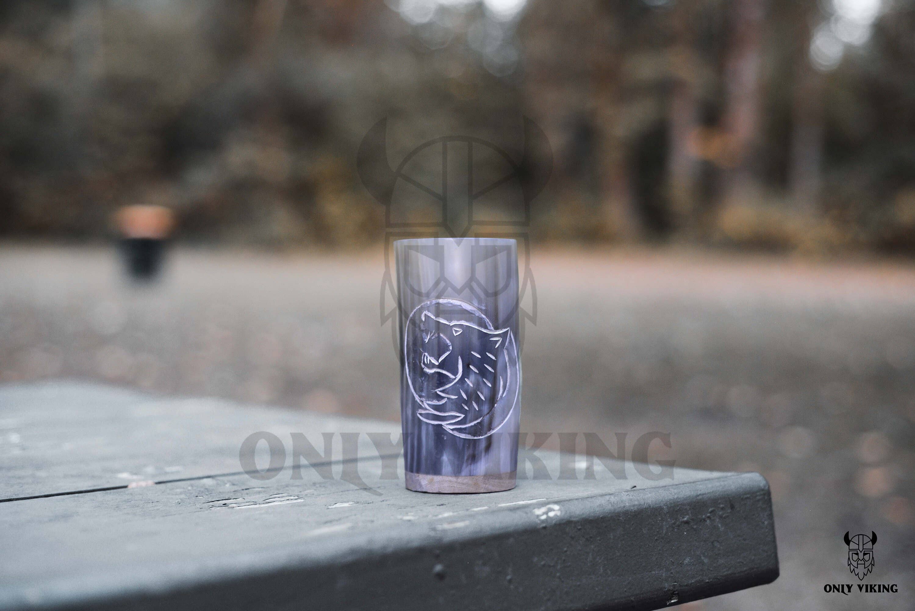 The Horn Mug: Beer Stein Drinking Horn Mug Tree of Life 6-9 oz rests on a wooden picnic table outdoors, set against a backdrop of blurred trees.