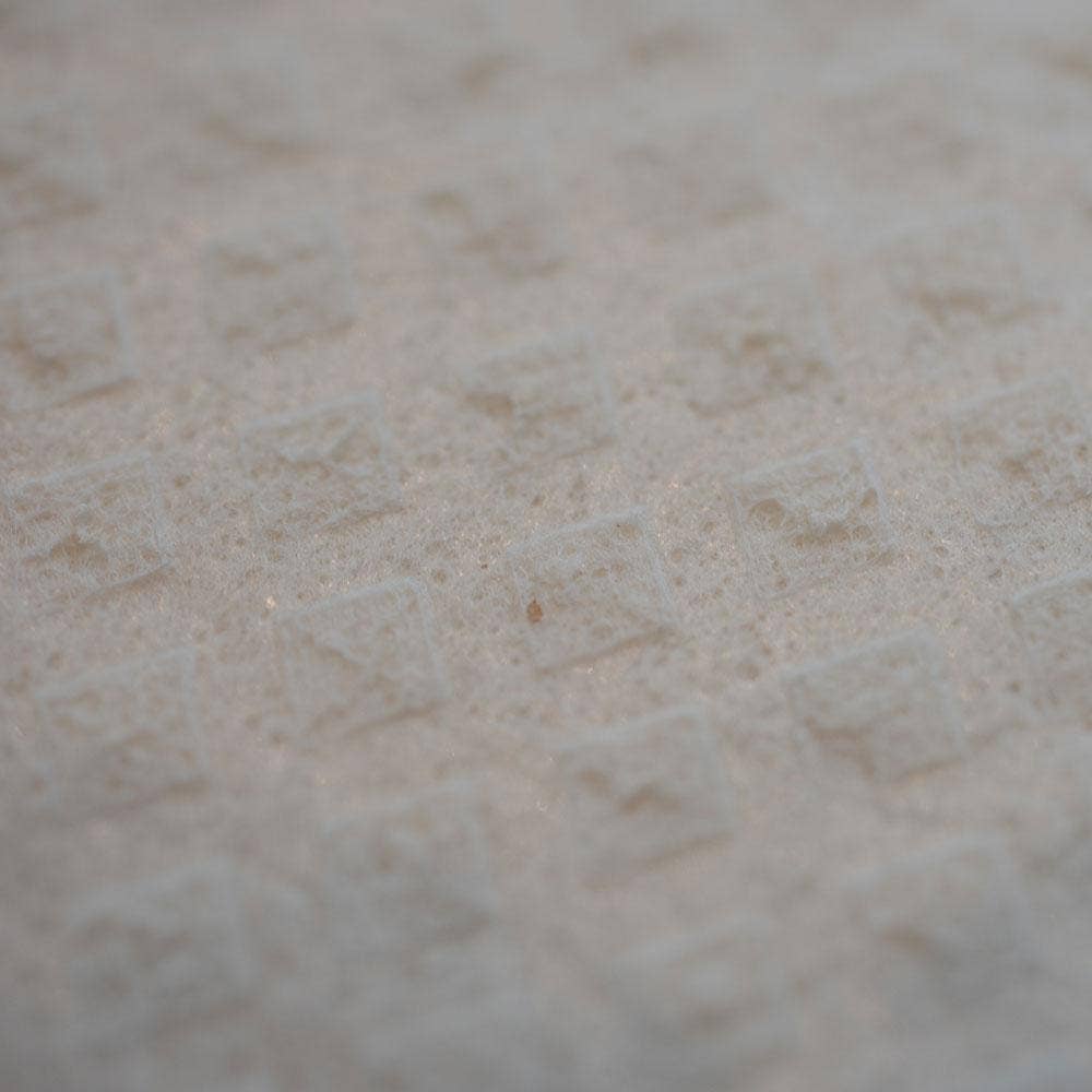 Close-up of a textured white surface with a repeating diamond pattern, similar to the weave on the Swedish Dishcloth: Christmas Three Gnomes.