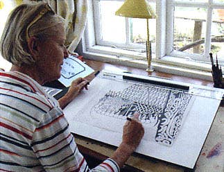 A person with short gray hair sits at a desk, drawing an intricate pattern. Theyre surrounded by a window, lamp, and drawing tools, while Dala Horse with White Flowers by Heidi Lange Framed (11x14) decorates the wall.