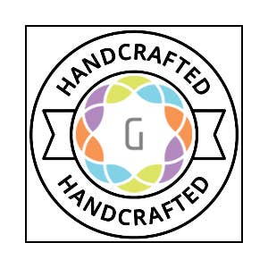 A circular badge with HANDCRAFTED at the top and bottom, featuring a multicolored wreath and a gray G—ideal for highlighting Earrings: Ruby Red Swarovski Crystal Handmade Silver Solitaire Stud Earrings.