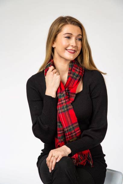 Woman with long light brown hair wearing a black sweater and a Royal Stewart Lambswool Scarf, sitting and smiling against a plain background.