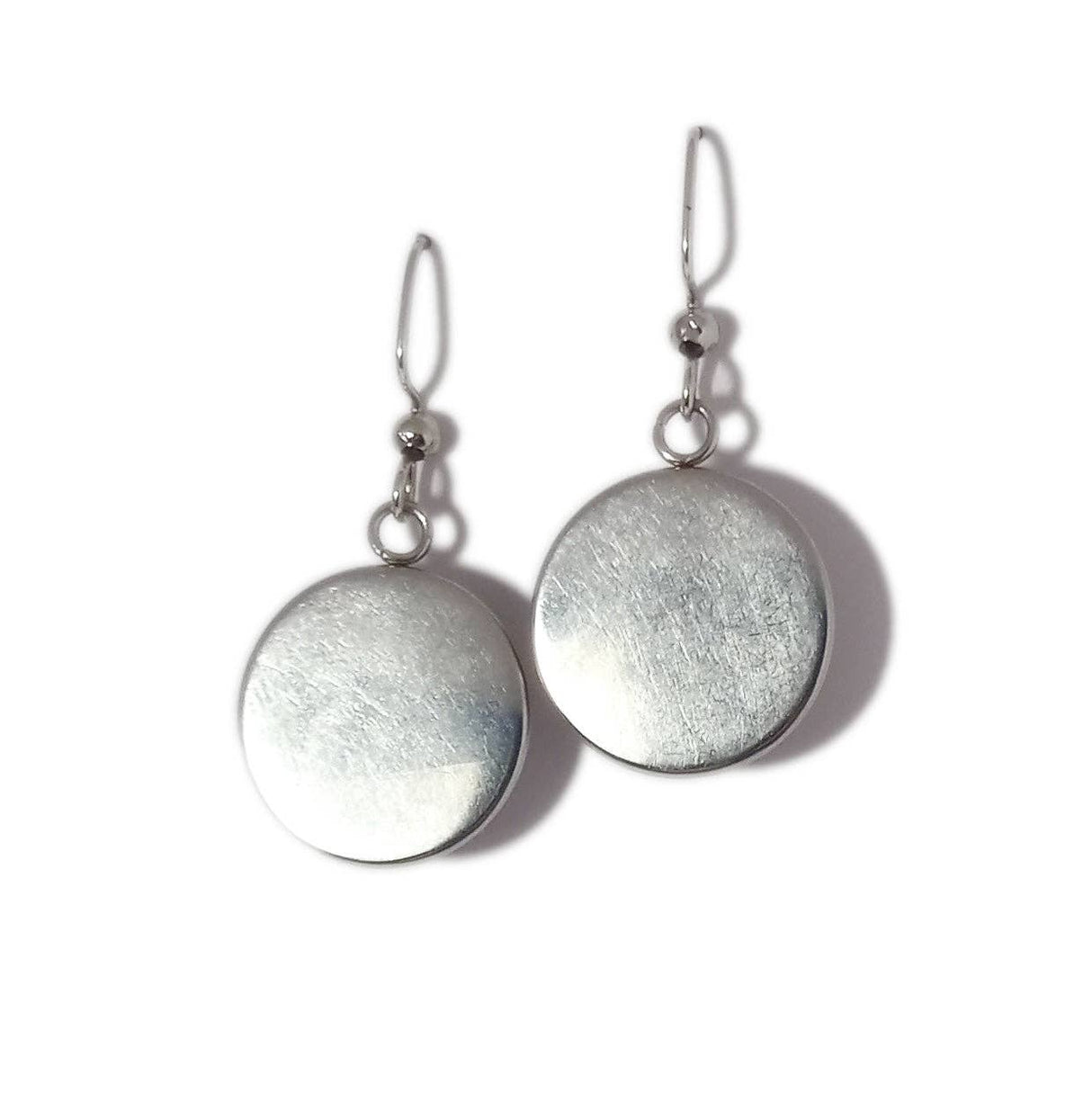 The "Mushrooms" earrings by Sarah Angst feature handmade silver round discs with hooks, gleaming against a white background and showcasing the artisan's craftsmanship.