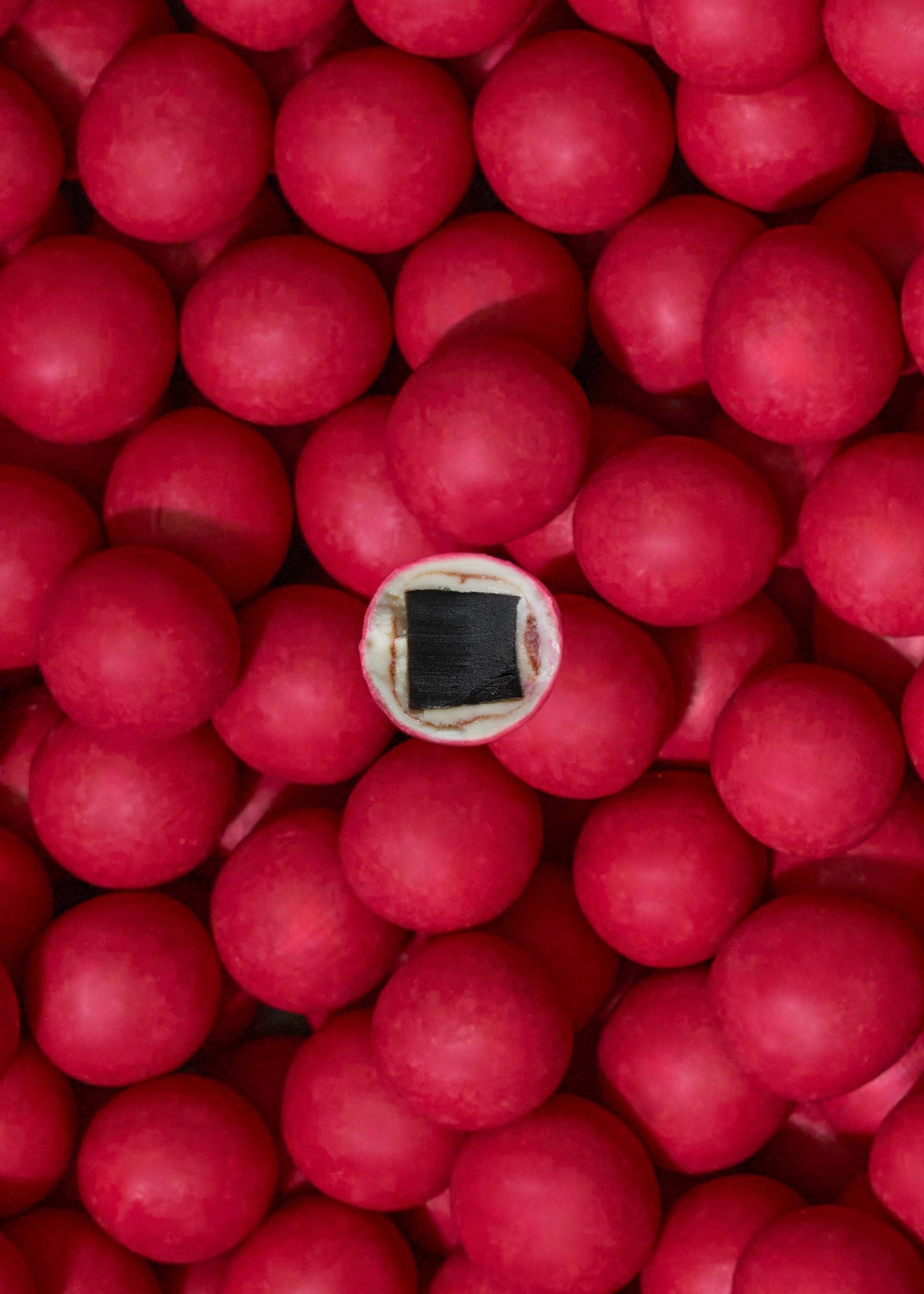 A group of red gumballs, one sliced to show a black licorice center, highlights Lakrids by Bülow - Strawberries & Cream Danish Chocolate Coated Licorice (125g), a limited edition treat inspired by Danish love.