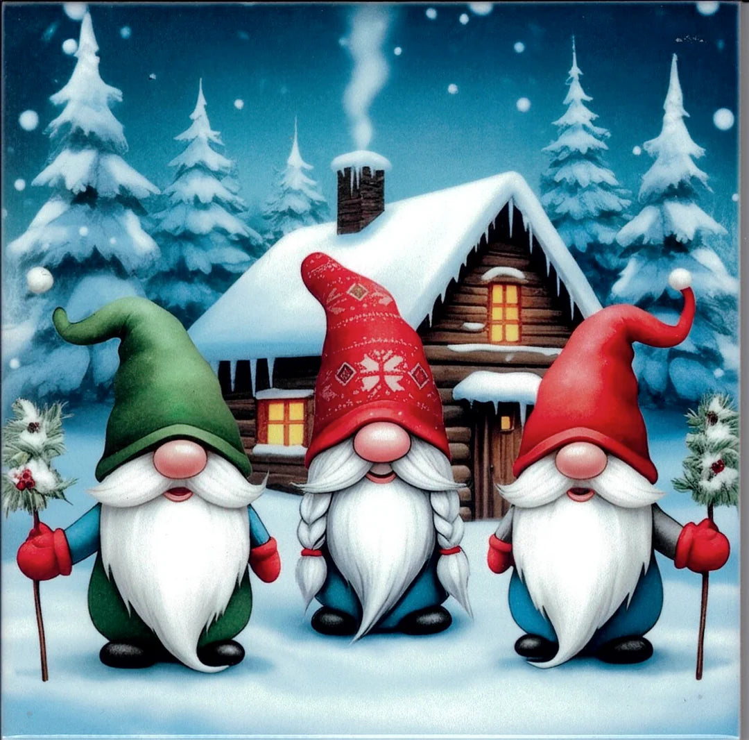 Three gnomes with white beards and red or green hats stand by a snowy cabin at night, making this 6" square Three Gnomes Ceramic Tile with cork backing & hanger perfect for Nordic Christmas decor.