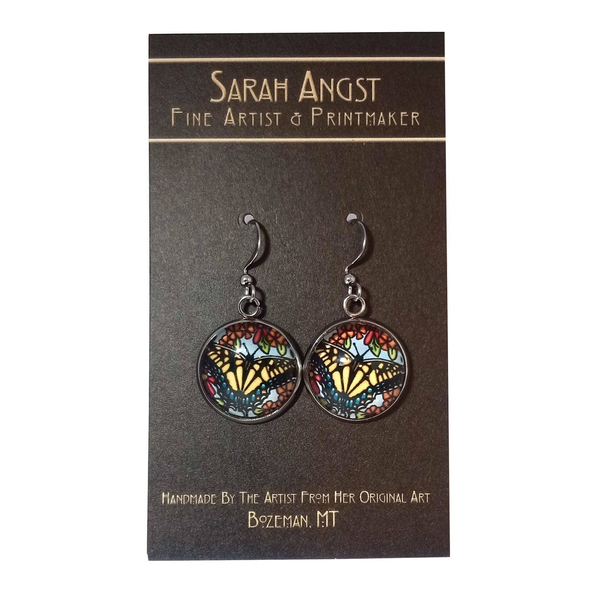 These handmade Swallowtail Butterfly earrings by Sarah Angst showcase intricate stained glass butterfly designs. Crafted with meticulous attention to detail, they come displayed on a card labeled "Sarah Angst Art, Fine Artist & Printmaker," capturing the essence of unique artistry from Bozeman, MT.