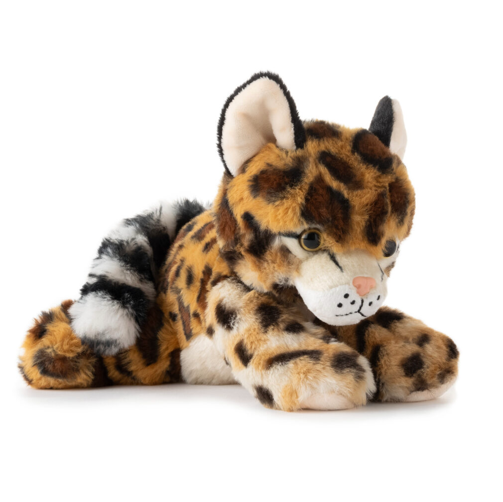 Plush ocelot with spotted fur, white and black striped tail, and large round eyes lying on a white background.