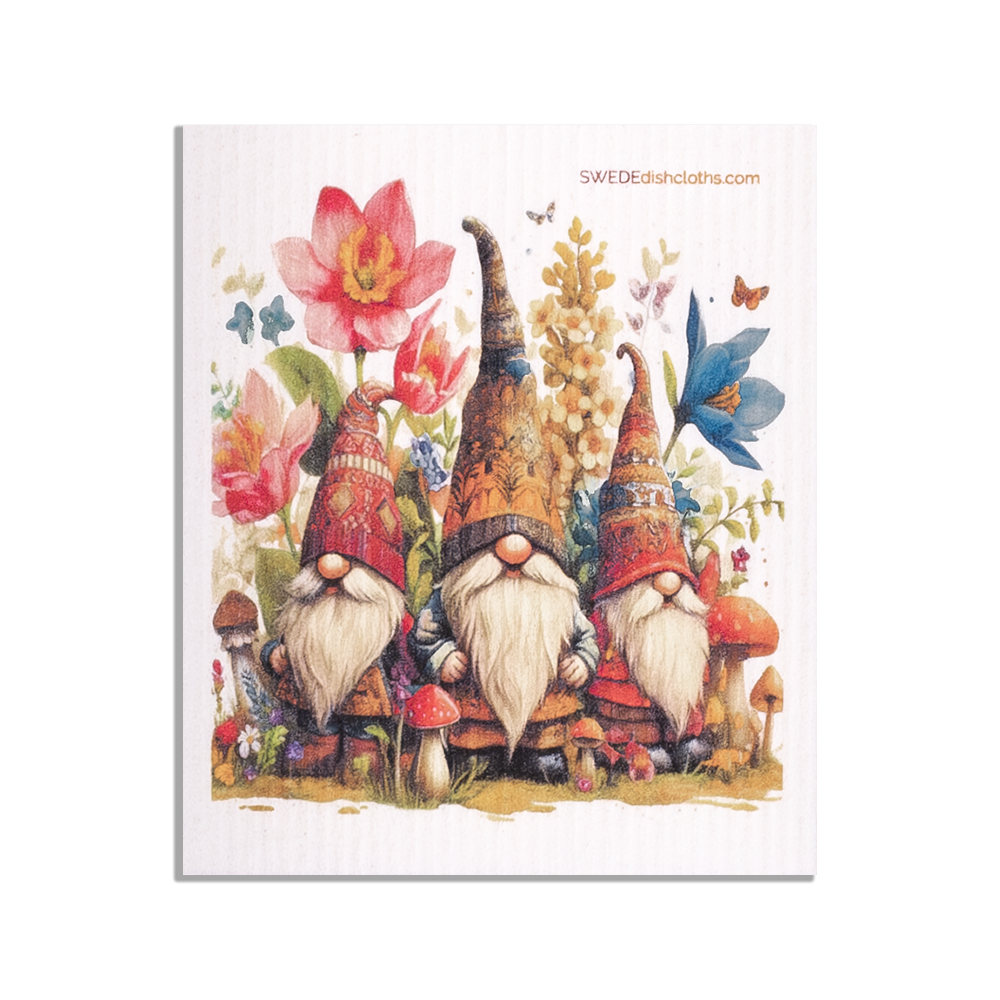 Three gnomes with long white beards and tall hats sit among bright flowers and mushrooms as a butterfly flutters above—beautifully featured on this eco-friendly Swedish Dish Cloth: Gnomes with Butterflies.