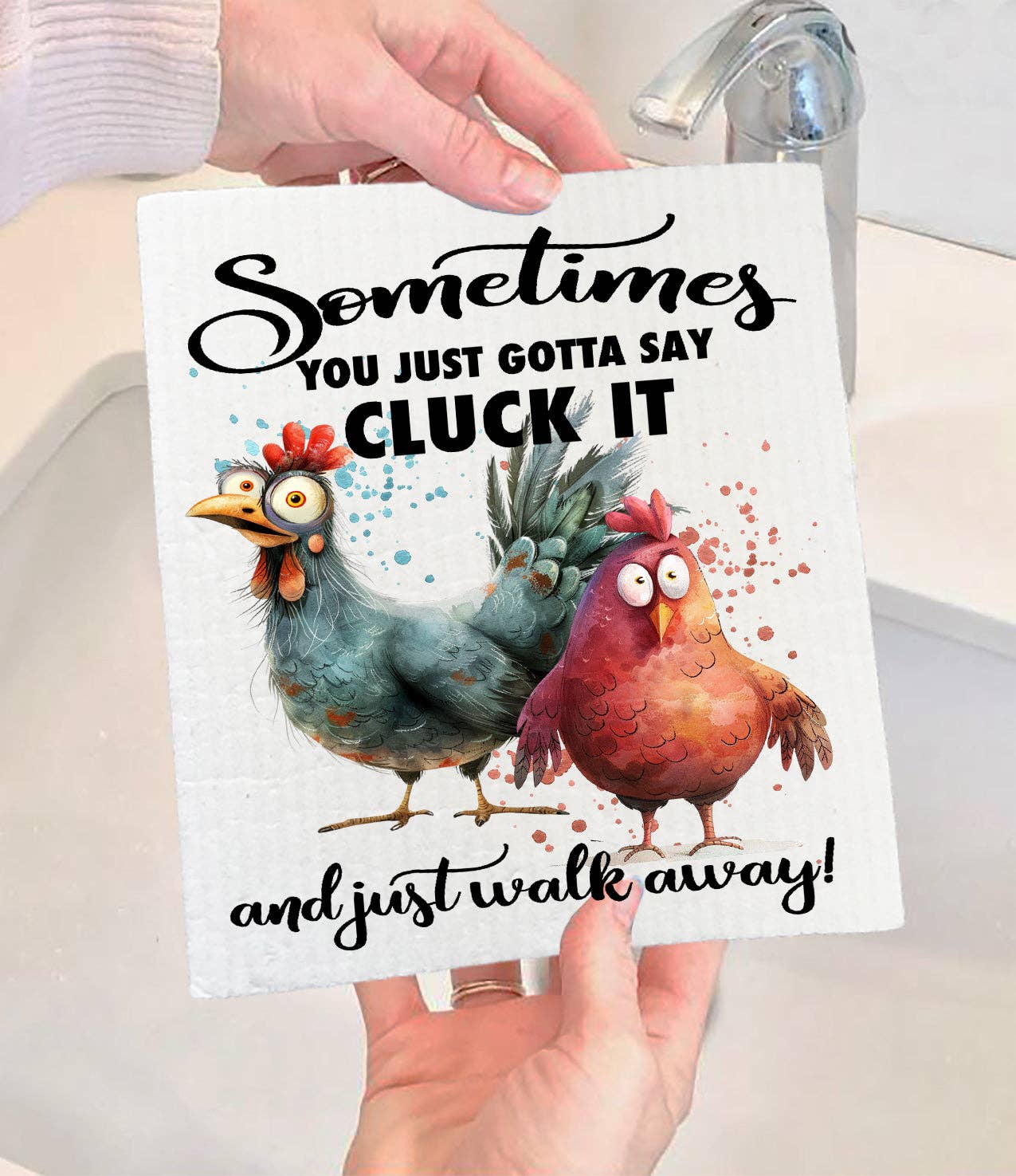 Someone holds the Dish Cloth: Gotta Cluck it and Walk Away Chickens Swedish Dishcloth—an eco-friendly cloth featuring cartoon chickens and the phrase Sometimes you just gotta say cluck it and just walk away!—near a sink.