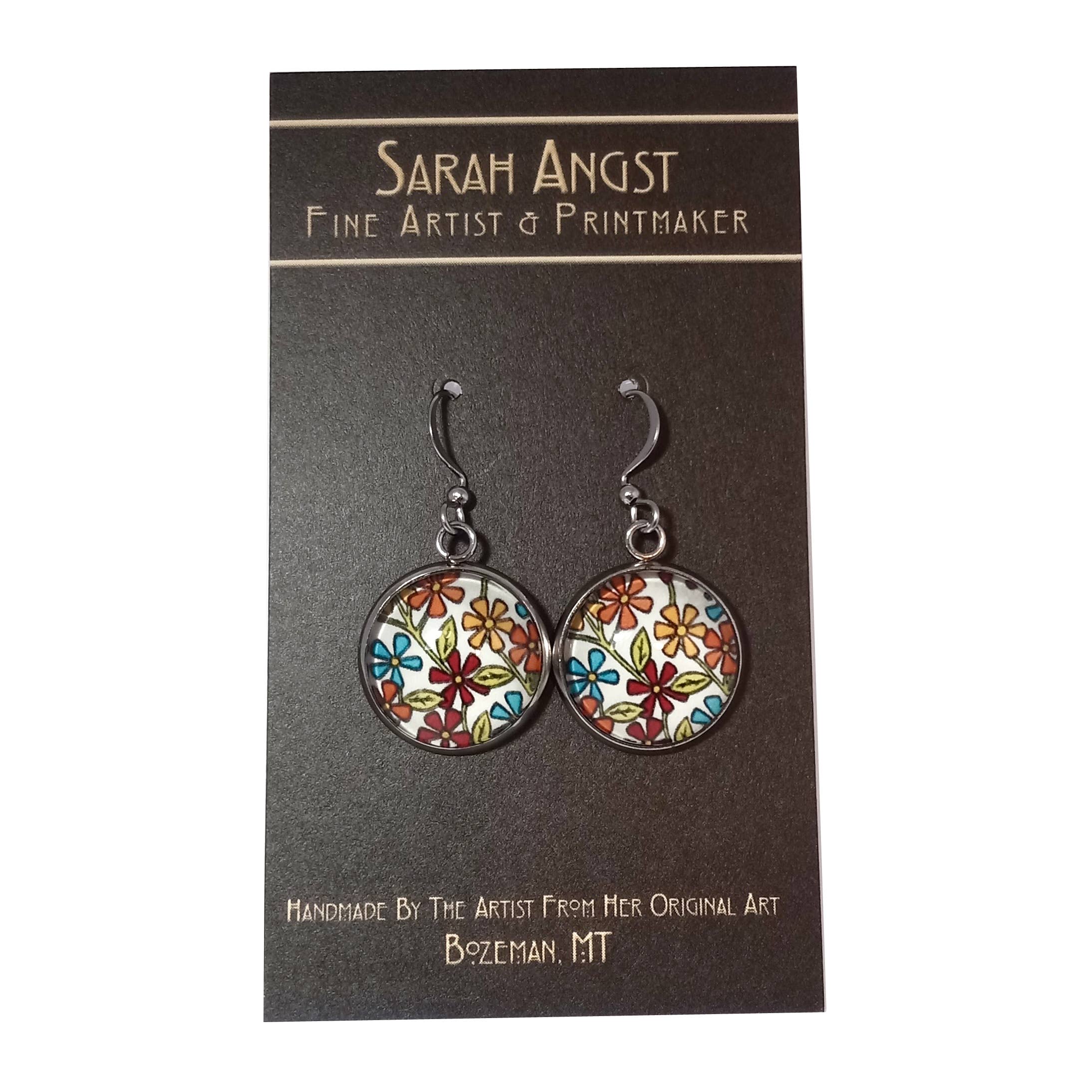 These "Earrings: Flowers on White by Sarah Angst" feature a colorful floral mini giclee print on a card that reads Sarah Angst Art, Fine Artist & Printmaker, handmade in Bozeman, MT.