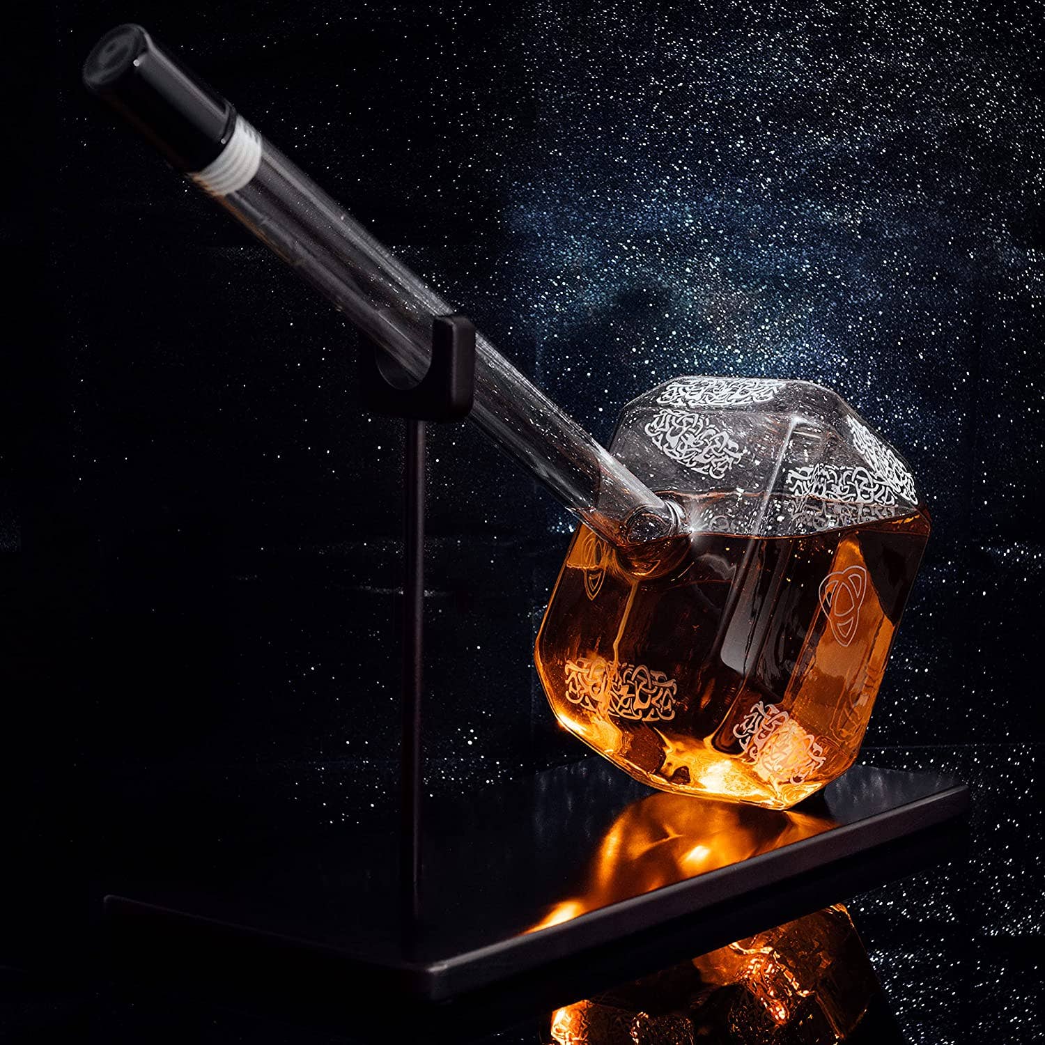 The Thor Hammer Whiskey and Wine Decanter 3500ml, filled with amber liquid, rests tilted on a black stand against a starry backdrop, adding Norse mythology flair to your barware collection.