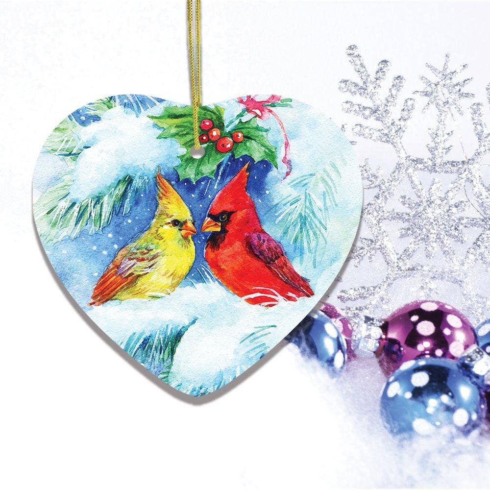 The Watercolor Cardinal Mistletoe Romance Christmas Heart Shaped Ornament features a cardinal amid holly, silver snowflakes, and colorful baubles on a white background, adding charm to a snowy scene.