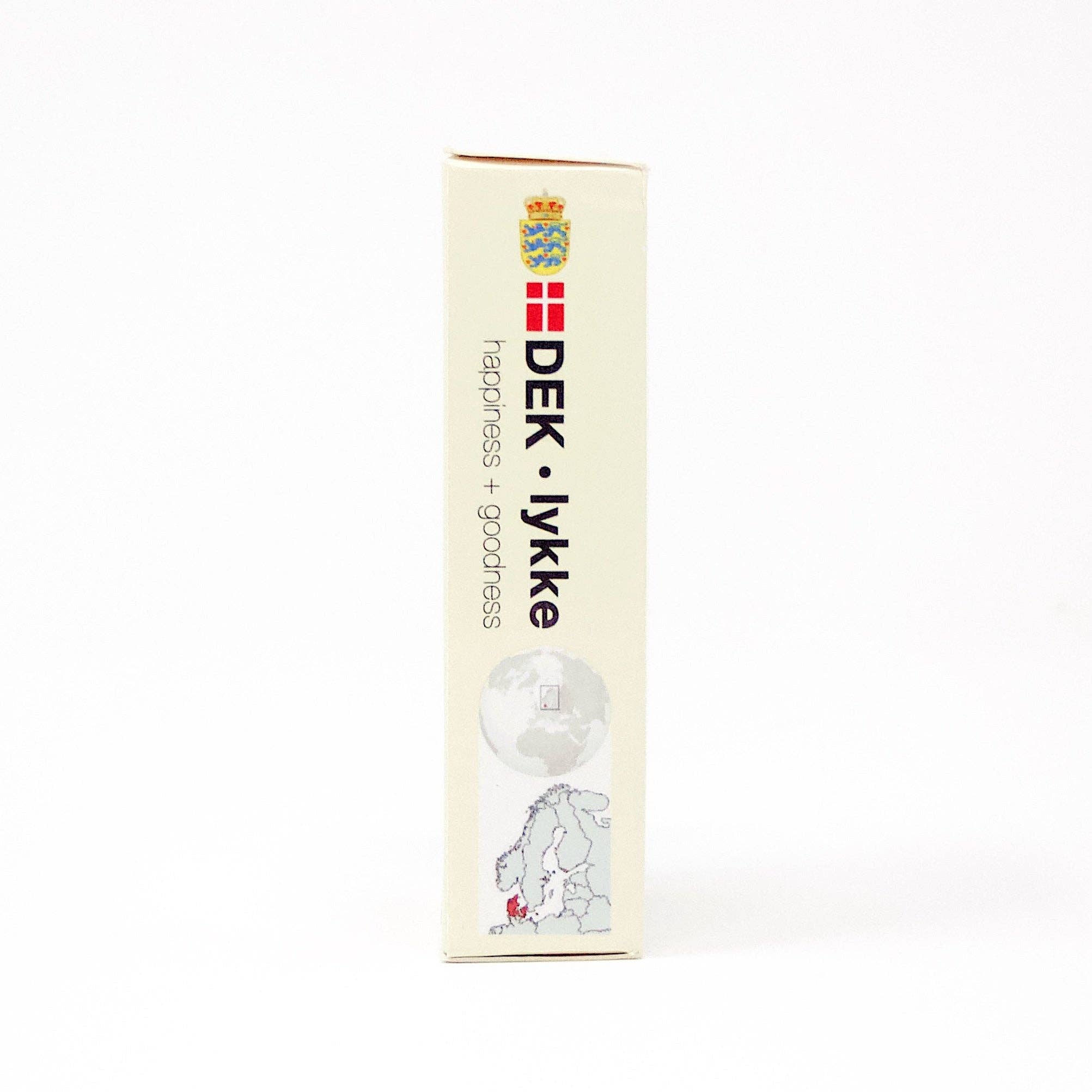 A white package prominently features the DEK Lykke (Denmark) label, complete with a Danish flag and crown emblem. The text enthusiastically communicates happiness + goodness, alongside an illustration of a globe with a continent outline, capturing the essence of Lykke.