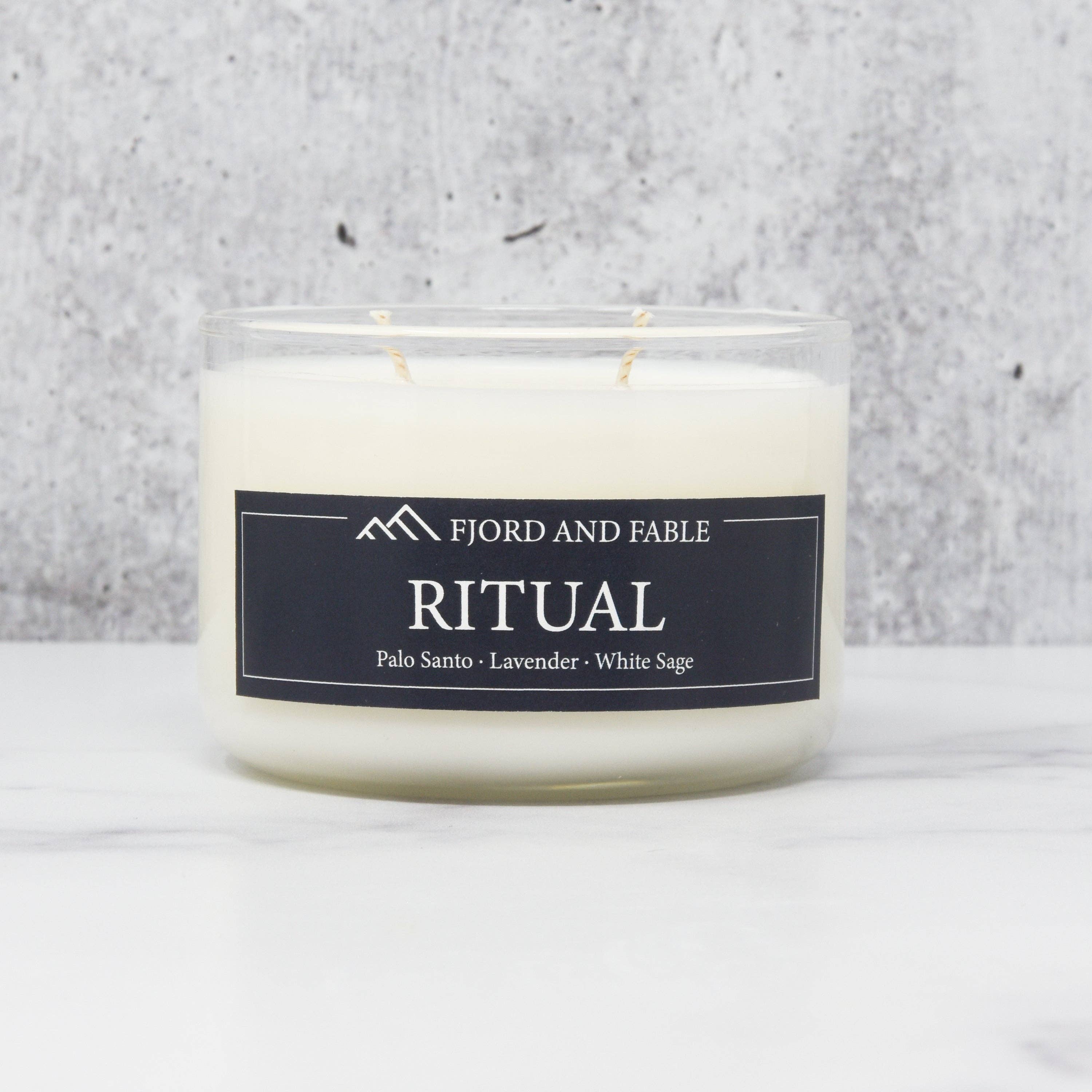 A 4oz white soy wax Ritual Candle by Fjord and Fable, scented with Palo Santo, Lavender, and White Sage, sits on a marble surface in its glass container.