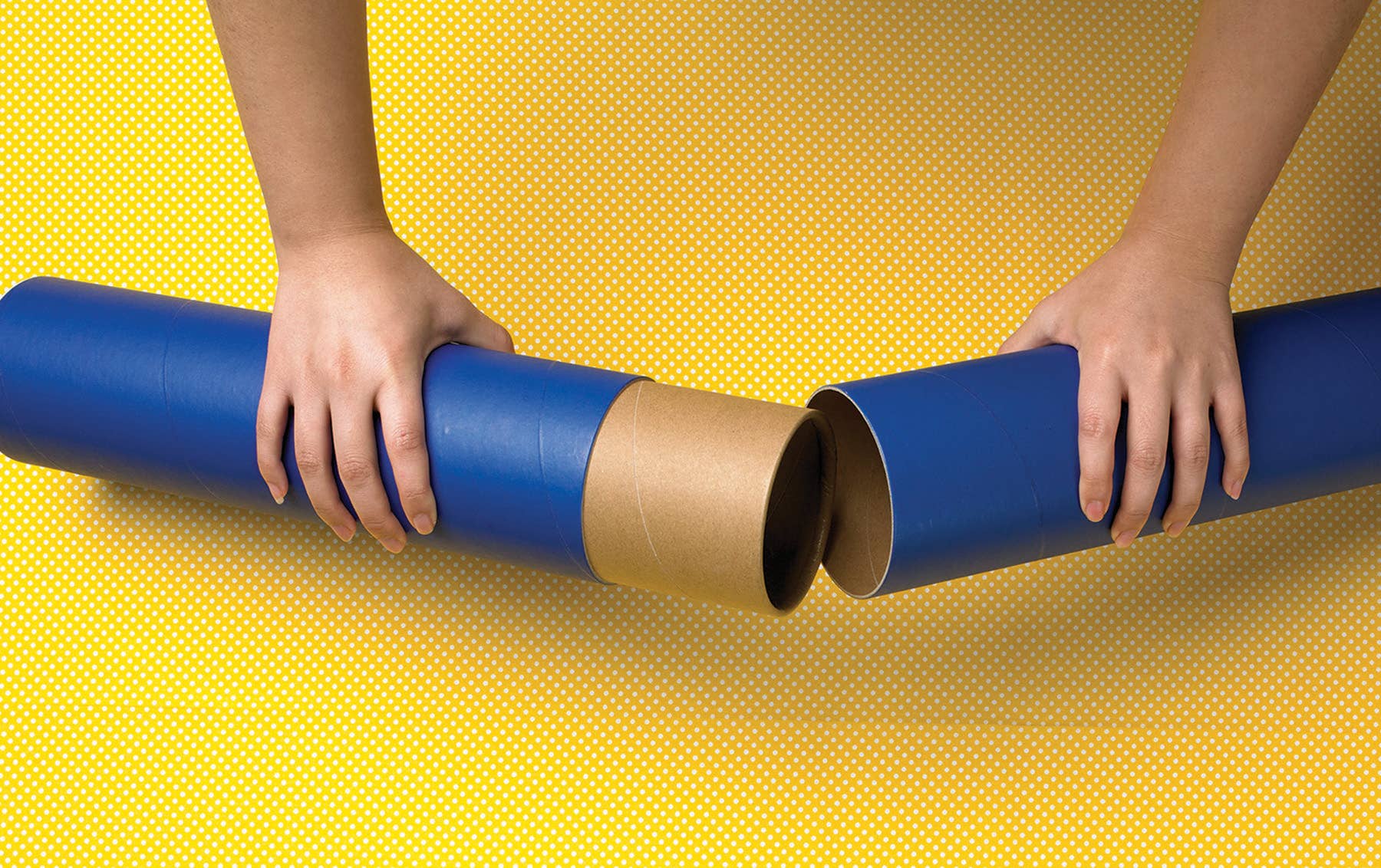 Two hands join two blue cylindrical tubes against a yellow background, reminiscent of assembling a Mat: Puzzle Roll Away Mat.