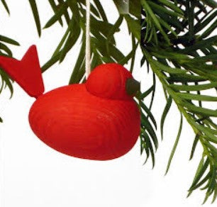 The Ornament: Red Wooden Bird, handcrafted in Sweden, dangles from a string amidst a backdrop of green leaves.