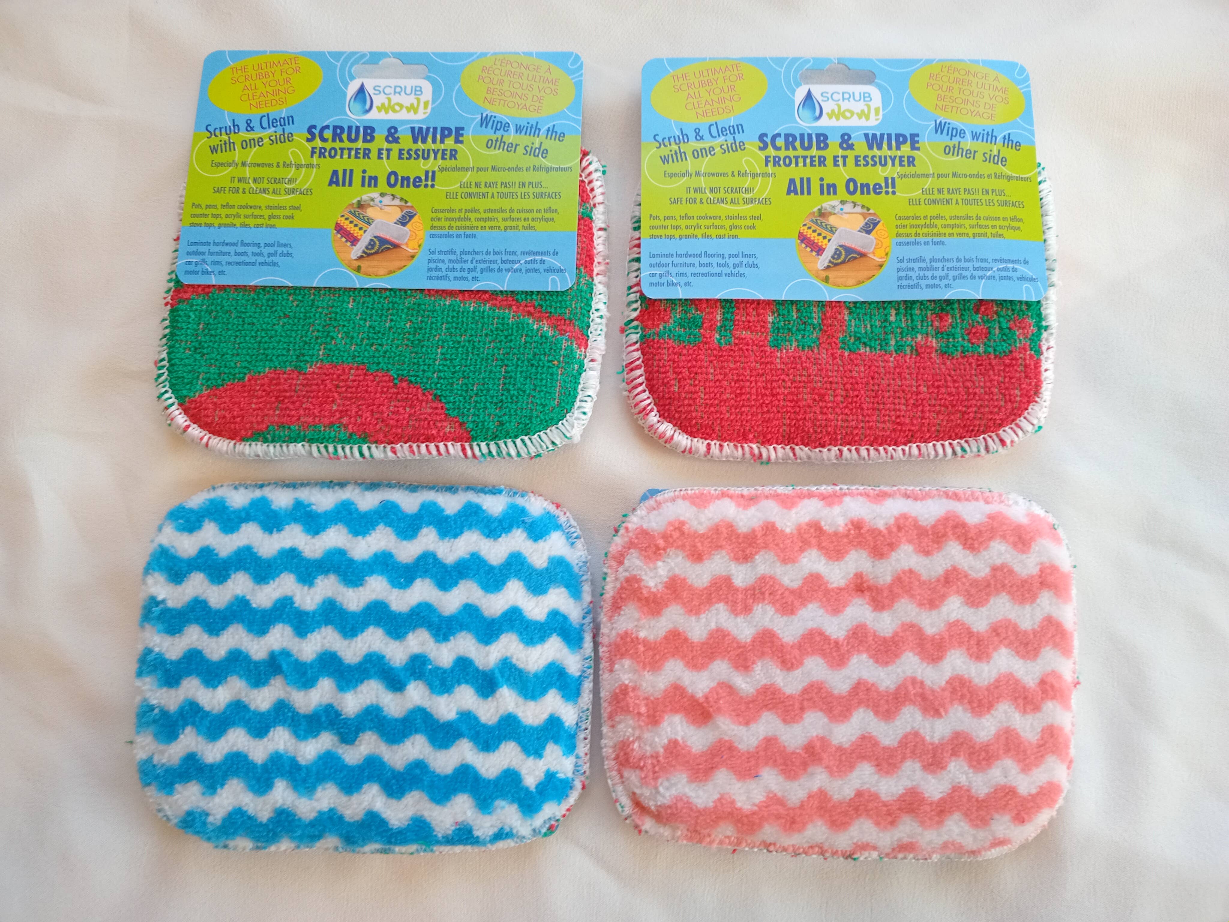 Four dual-sided Scrub: Scrub & Wipe Plus Sponges—two red/green, two blue/white zigzag—are shown on a white surface, top two with labels. Perfect for scrubbing and wiping surfaces during multi-purpose cleaning.