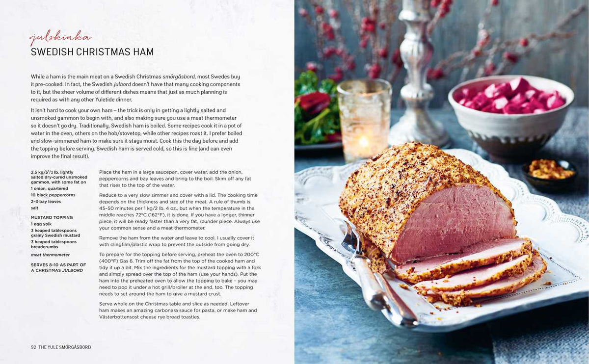 Sliced baked ham with a mustard and breadcrumb coating on a silver platter, Scandinavian style. Out-of-focus pink beet salad in the background.