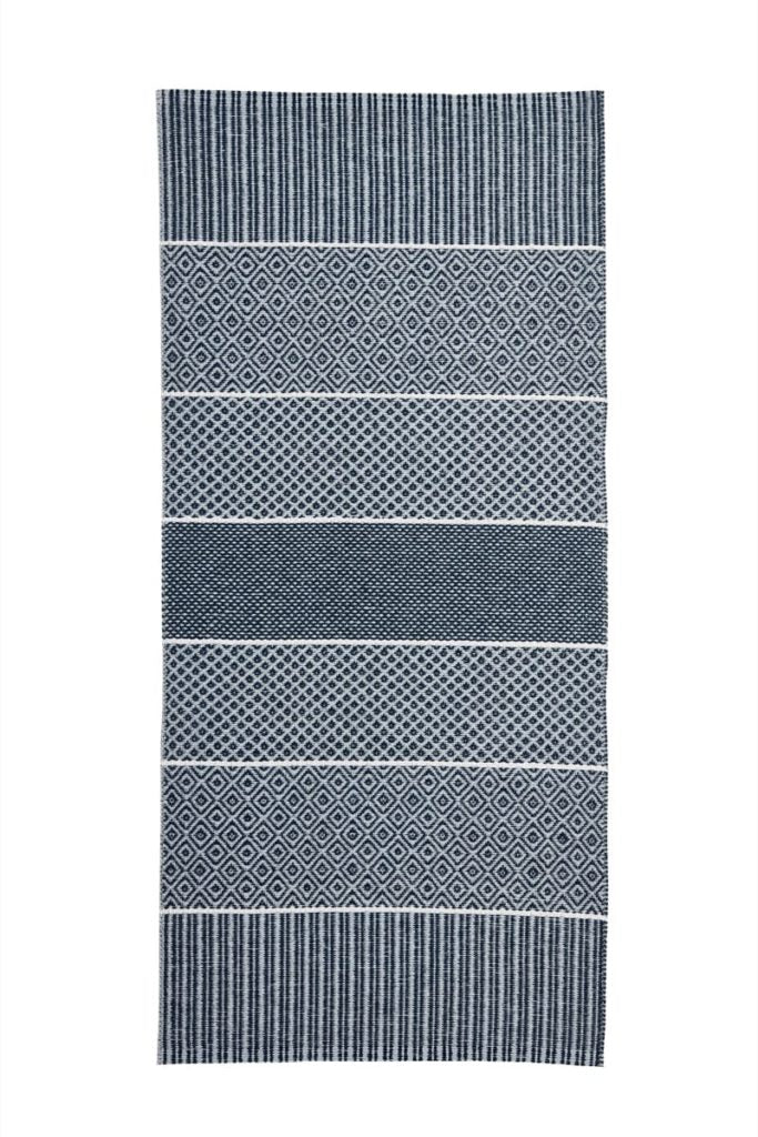 The Horredsmattan - Alfie vinyl rug is a blue Swedish creation that combines traditional woven vinyl craftsmanship with modern design, displaying alternating striped and diamond patterns.