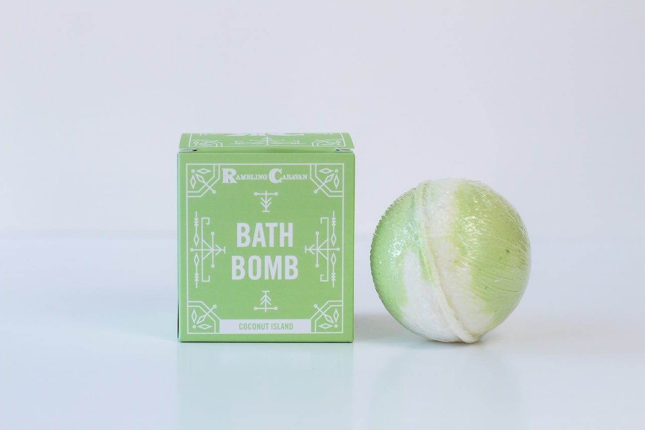A green and white Bath Bomb: Coconut Island with a skin-nourishing formula sits beside its matching green box, both placed on a white surface.