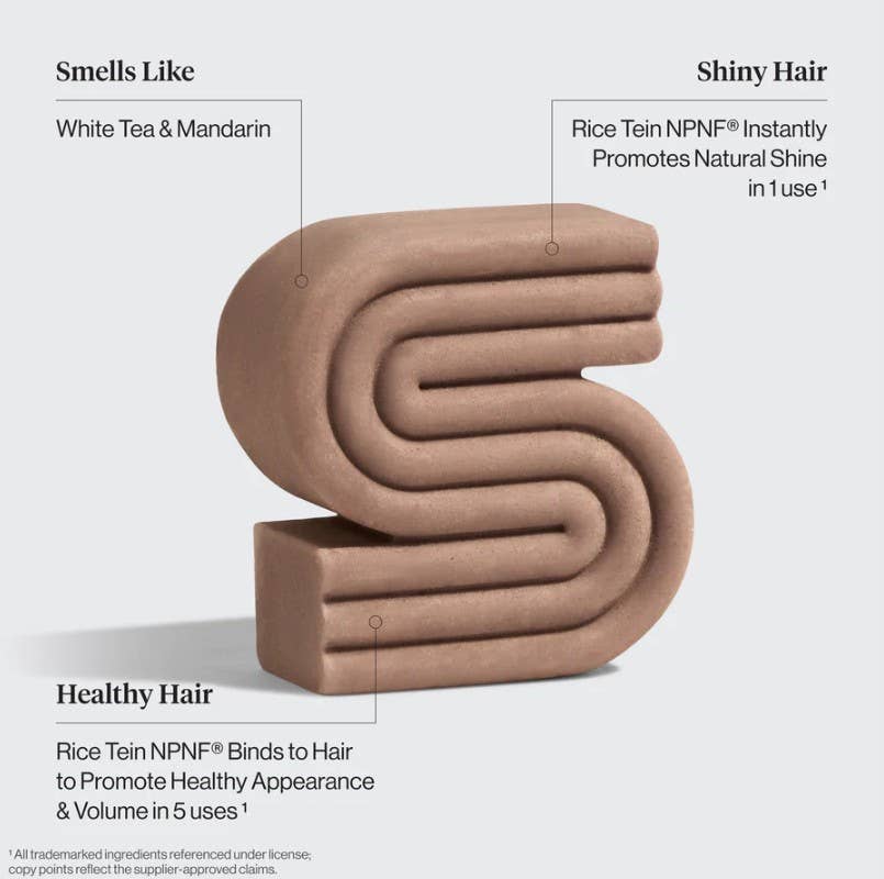 A brown, S-shaped KITSCH Rice Water Protein Solid Shampoo Bar for Hair Growth (3.2oz) is shown with labeled benefits: it features a refreshing white tea and mandarin scent, enhances hair shine after just one use, and supports healthy hair appearance and increased volume within five uses. This sustainable shampoo bar also helps boost hair volume while caring for the planet.