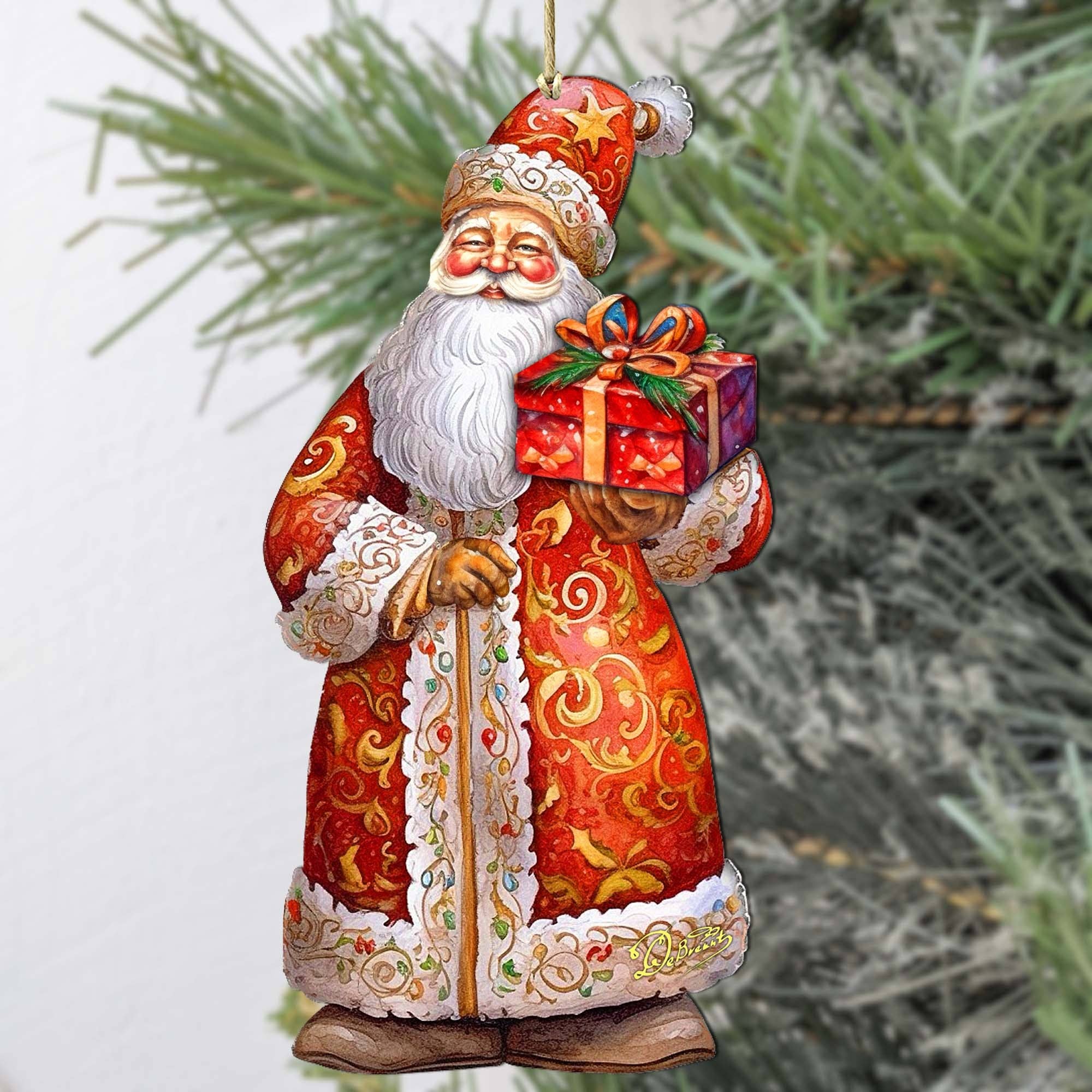 The St. Nick's Gift Wood Ornament by Artist G Debrekht, "Christmas Santa," features Santa in a red robe holding a present, crafted in classic G Debrekht style. Measures 5.5" tall x 3" wide—perfect for your Christmas tree.