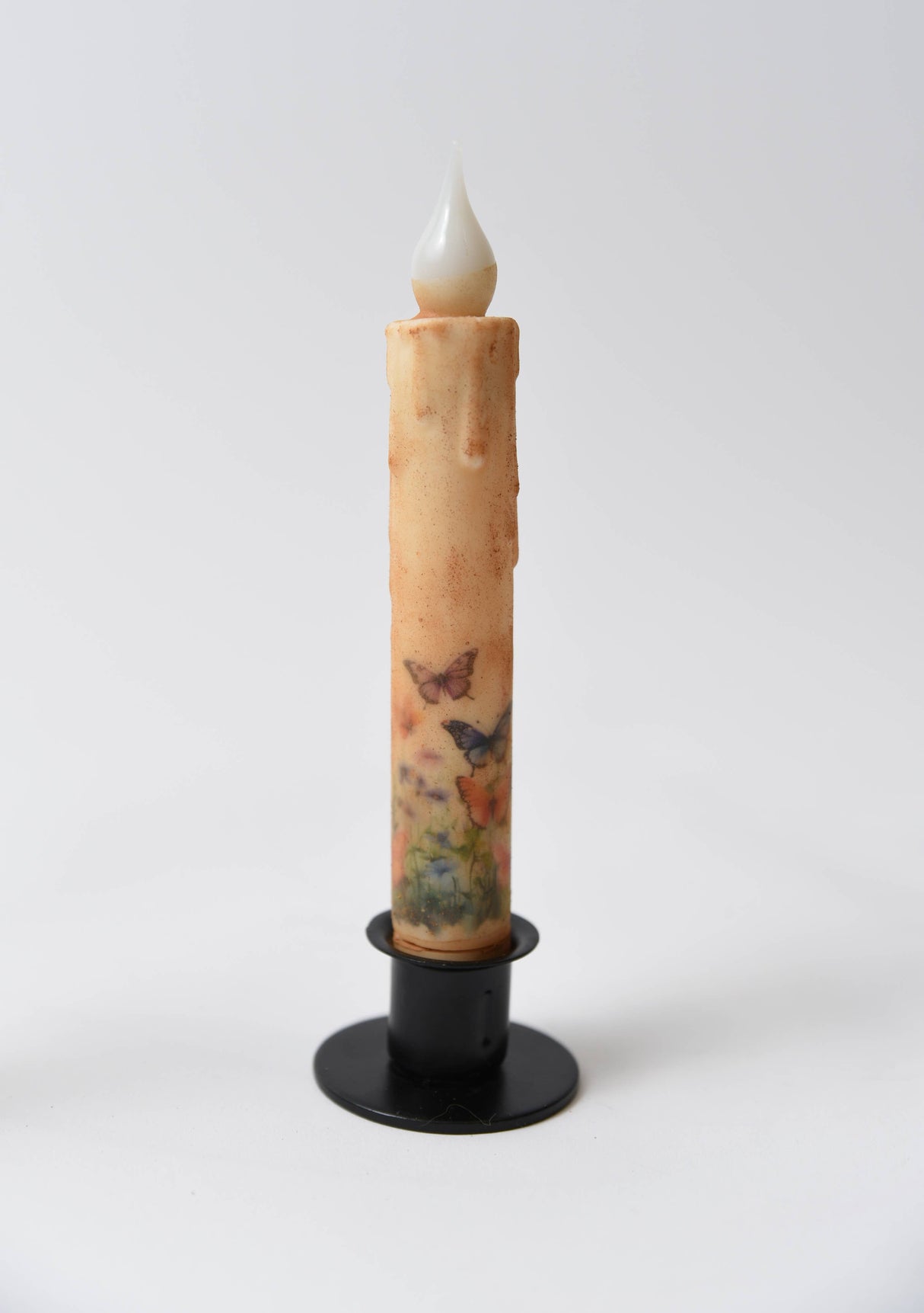 The Butterfly Panorama LED Timer Taper Candle: Top Dusted features a battery-operated design with butterfly and flower motifs, displayed in a black holder on a white background.