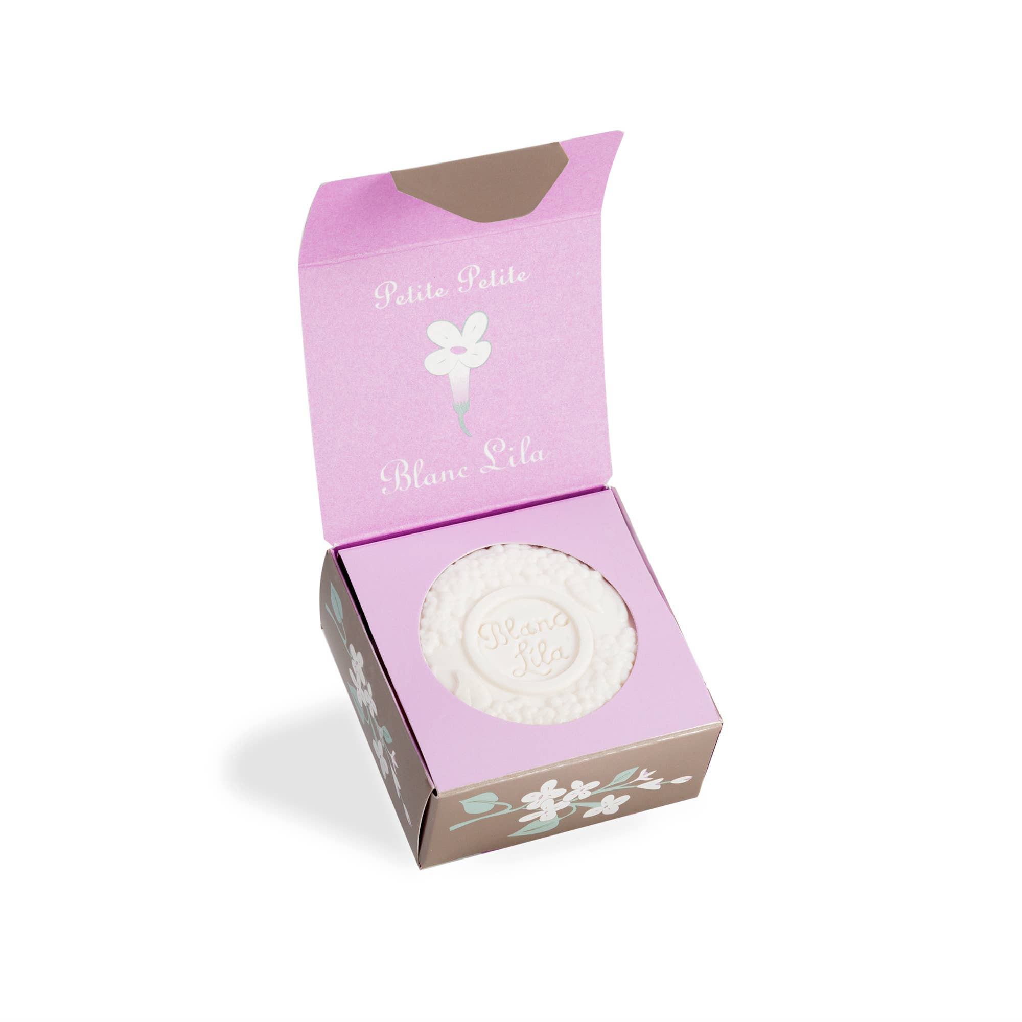 An open box presents the Petite Petite Blanc Lila Bar Soap, showcasing a round, white Lilac soap bar embossed with the text "Blanc Lila." The packaging is adorned with elegant purple and brown floral designs and prominently uses recycled materials, demonstrating a commitment to sustainability.