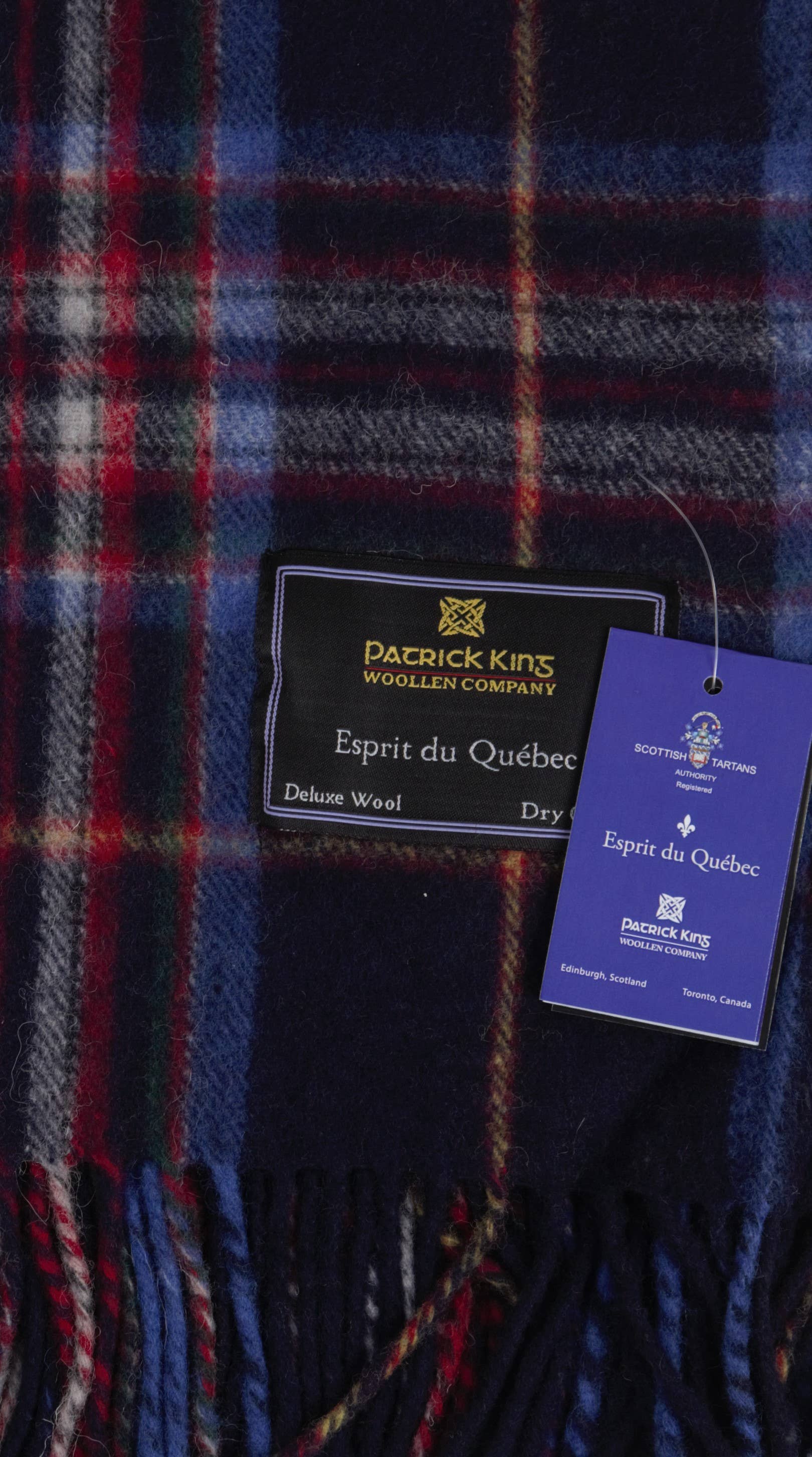 A close-up of the Esprit du Quebec Deluxe Highland Blanket from Patrick King Woollen Company shows tartan pattern and care tags attached.