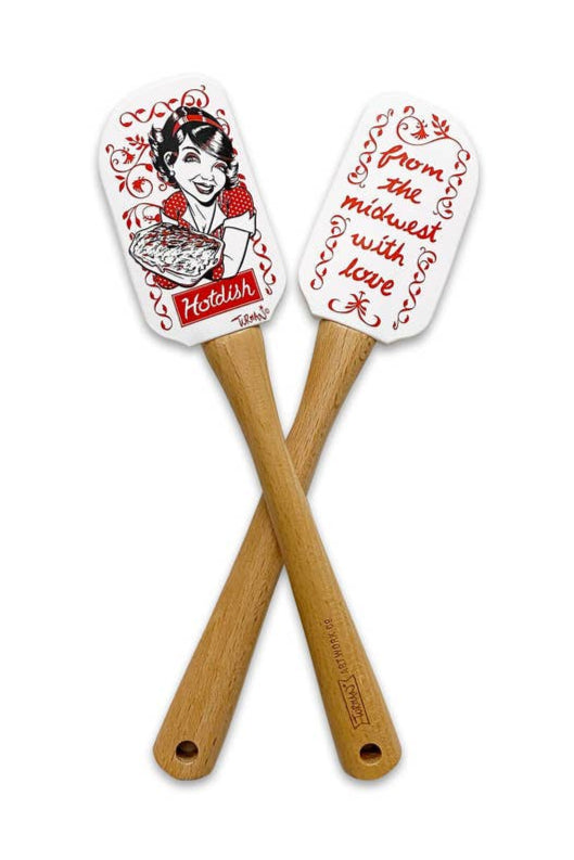 A pair of silicone spatulas with beechwood handles showcase decorative designs: one includes an illustration of a woman alongside the hotdish design, while the other is inscribed with "from the Midwest with love." This set is part of the product line named Dishware: Spatula Hot Dish.