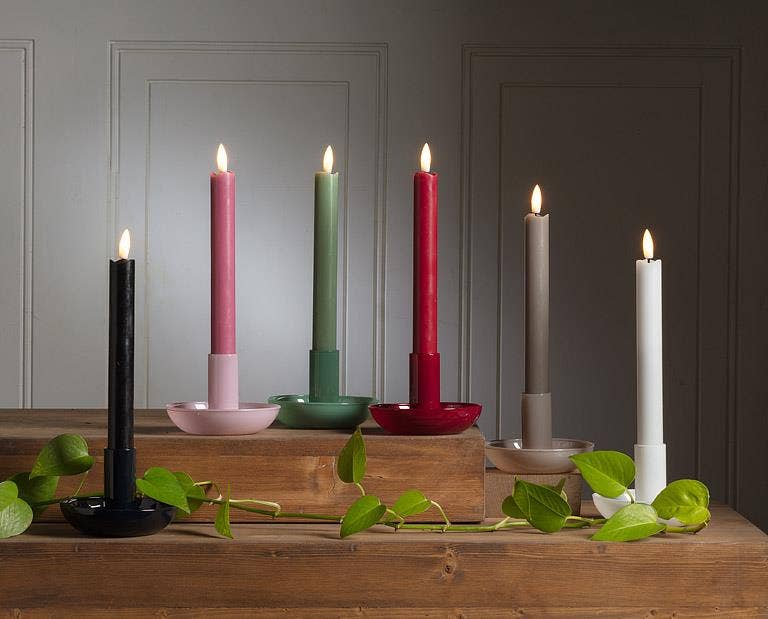 A red Small Pipe Taper Holder (2"H) displays a lit candle on wooden steps beside a green vine, creating modern decor that adds warmth and style to any space.
