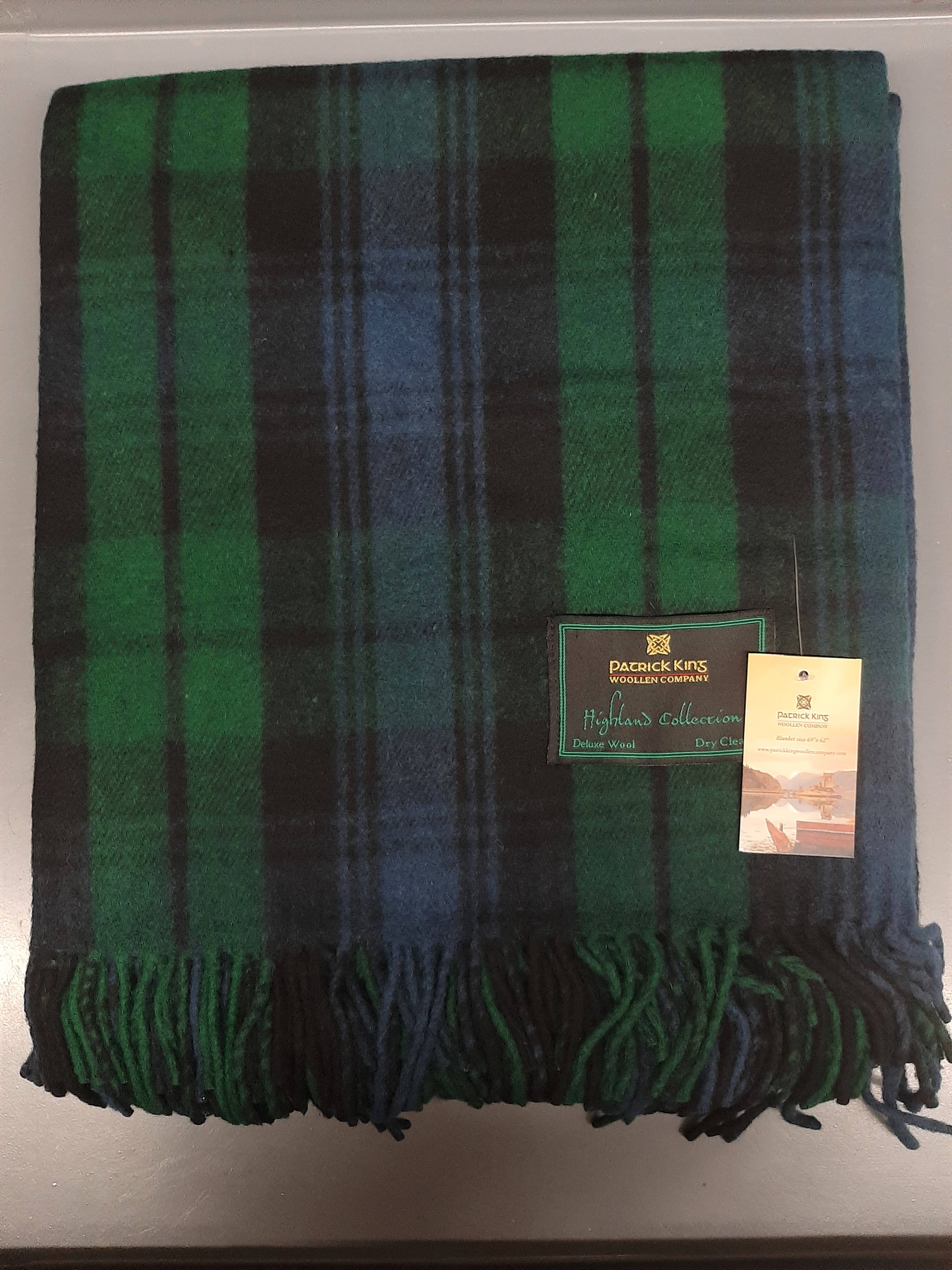 The Blanket: Black Watch Highland Blanket is a folded green and blue tartan plaid merino wool blanket with two labels, including one for Patrick King Highland Collection—perfect for adding warmth and style to any space.
