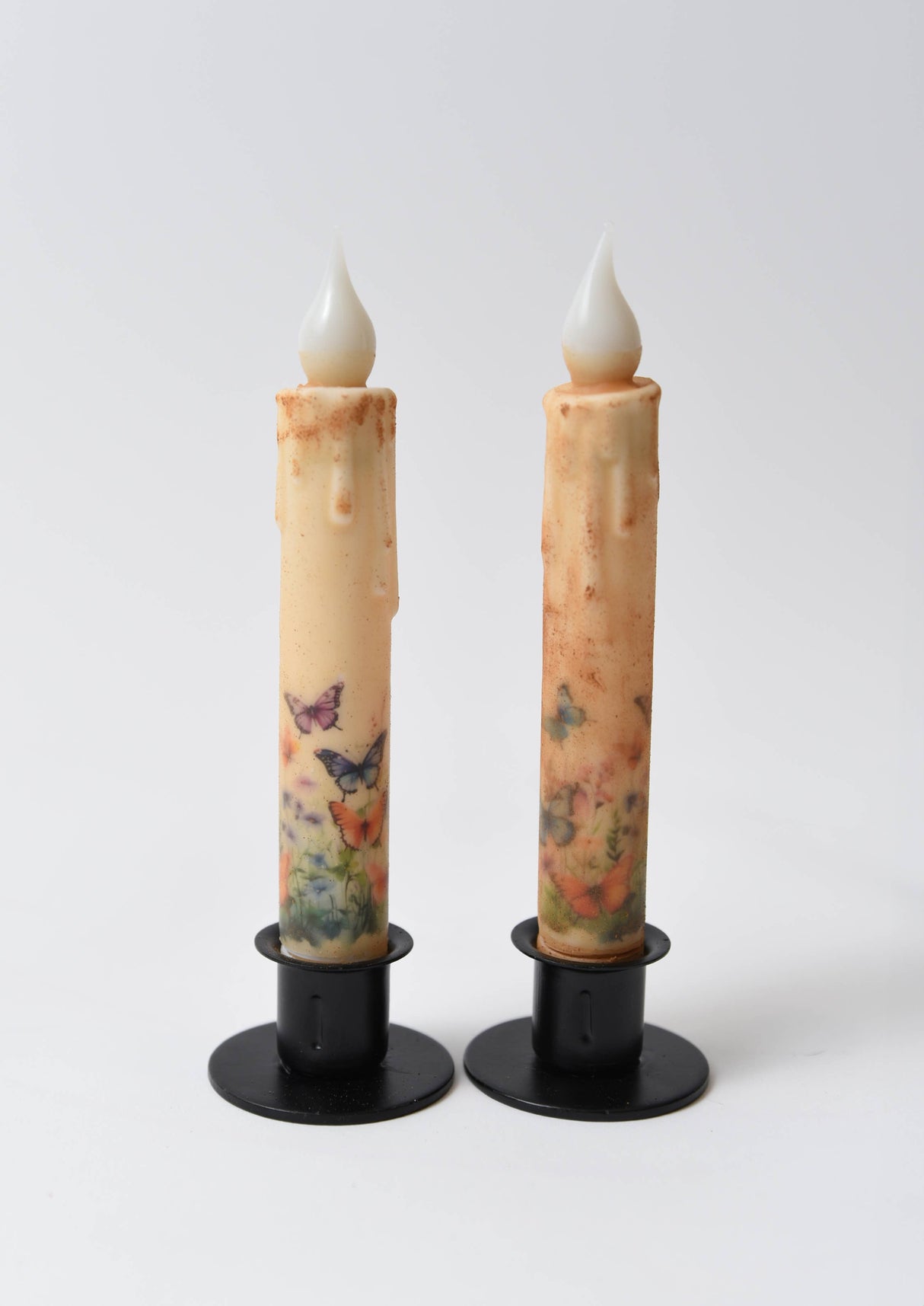 The Candle: Butterfly Panorama LED Timer Taper Candle: Top Dusted features two LED tapers with floral and butterfly designs on black bases, creating a charming butterfly panorama effect against a white background.