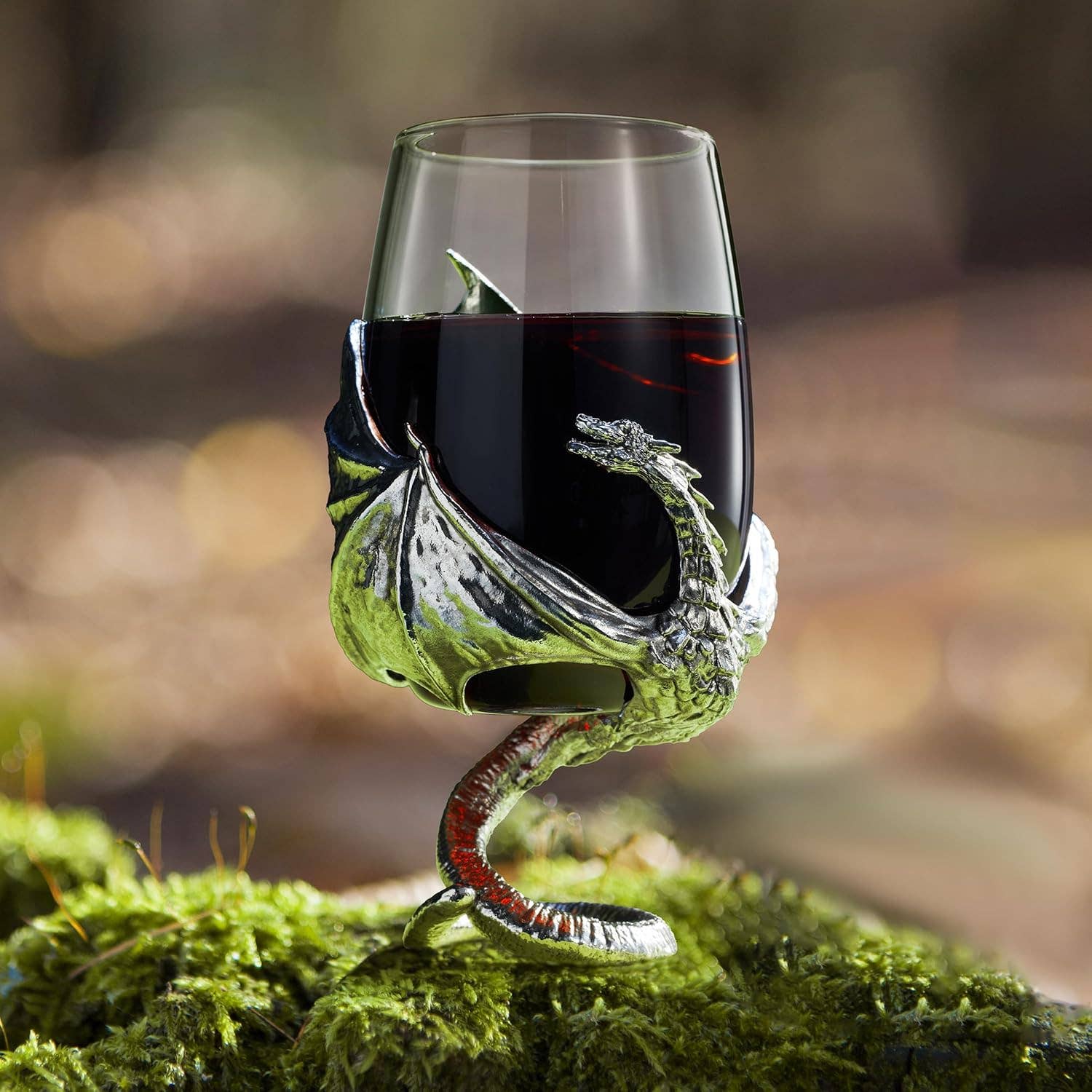 The Goblet: Medieval Dragon Viking Goblet Mug, 12oz features a metallic dragon-shaped stem and base, cradling red wine in fantasy drinkware style as it sits on moss outdoors.
